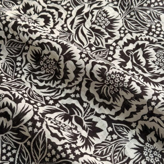 a close-up view of a fabric with a black and white floral pattern. The pattern consists of various flowers and leaves, creating a visually striking and intricate design.