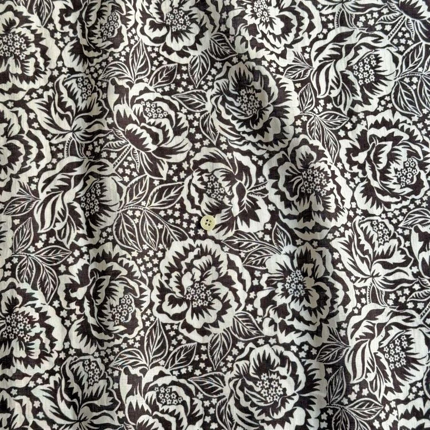 a close-up view of a fabric with a black and white floral pattern. The pattern consists of numerous flowers and leaves, creating a visually striking and intricate design. The fabric appears to be made of a material that has a textured surface, adding depth and dimension to the overall appearance.