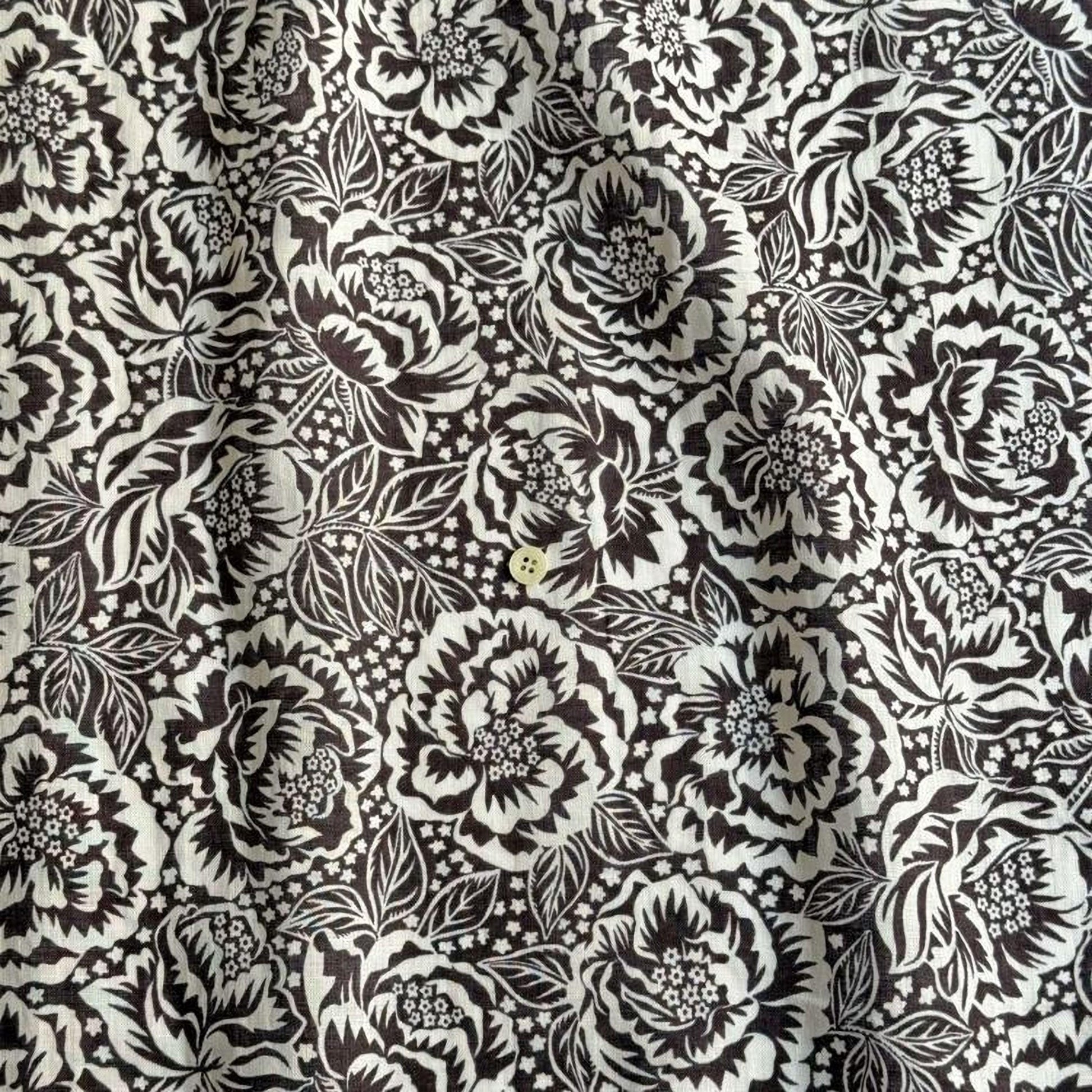 a close-up view of a fabric with a black and white floral pattern. The pattern consists of numerous flowers and leaves, creating a visually striking and intricate design. The fabric appears to be made of a material that has a textured surface, adding depth and dimension to the overall appearance.