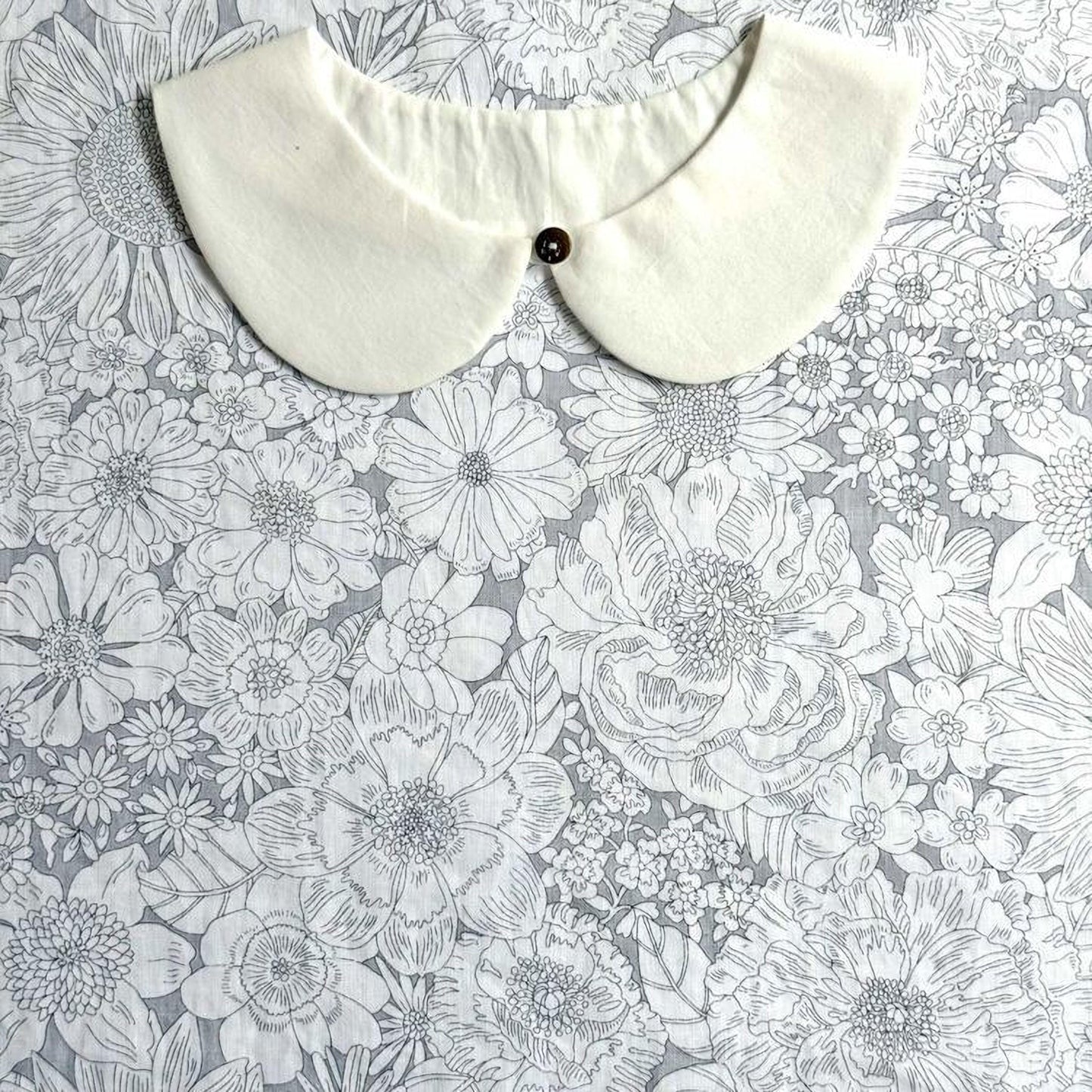 a white collar with a button, placed on a background with a floral pattern.