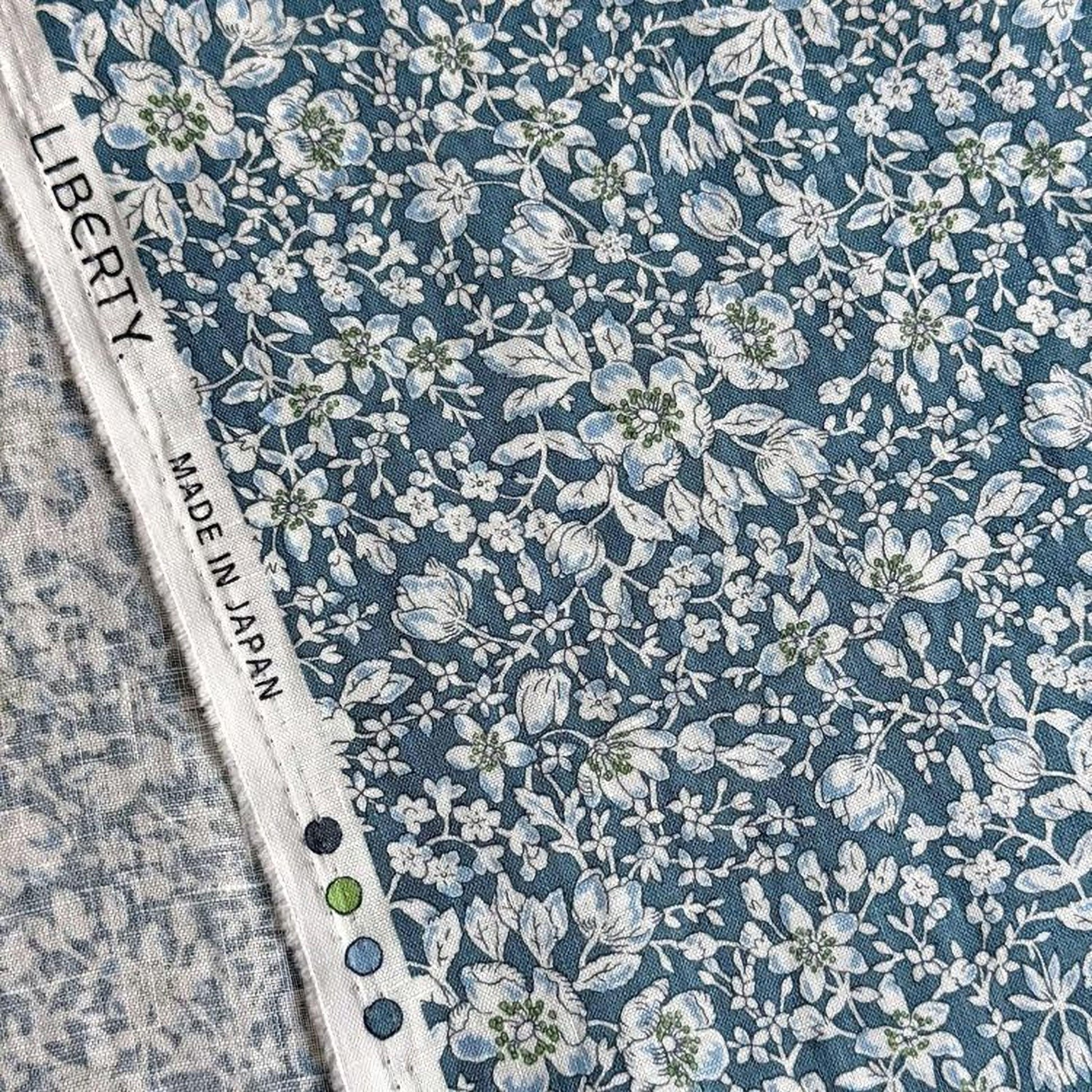 a close-up view of a fabric with a blue floral pattern. The fabric appears to be made of a material with a blue and white color scheme, and the text "LIBERTY MADE IN JAPAN" is visible, indicating the origin of the fabric.