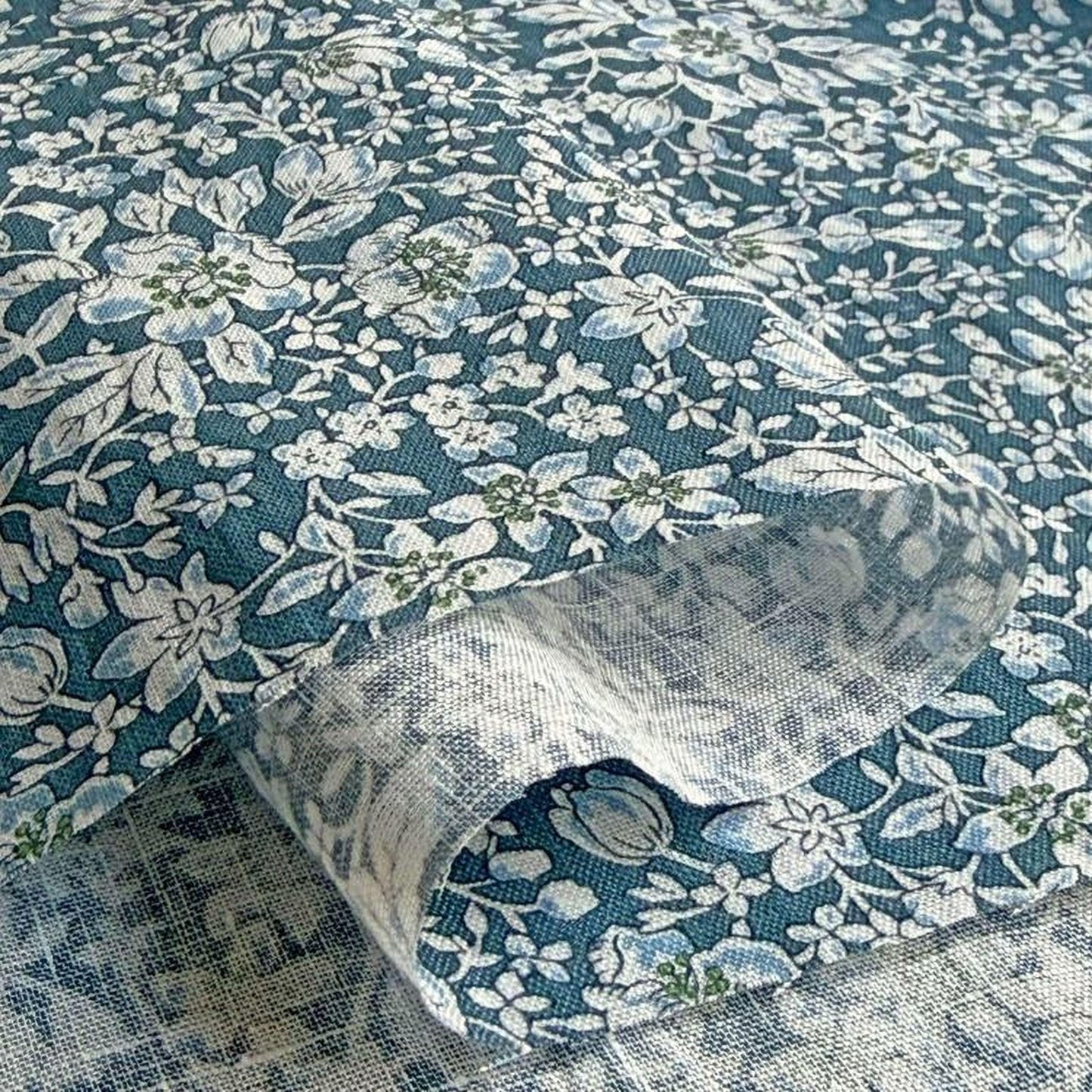 a close-up view of a fabric with a floral pattern in shades of blue and white. The fabric appears to be made of a soft, textured material, possibly cotton or linen. The pattern consists of various flowers and leaves, creating a visually appealing and intricate design.