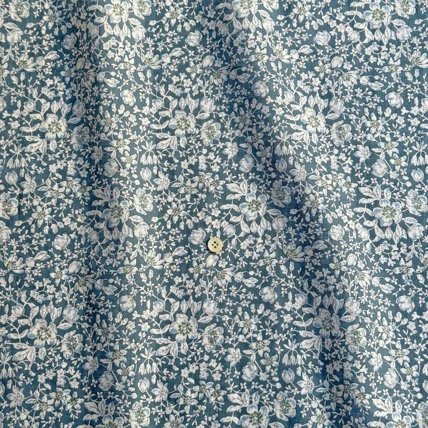 a close-up view of a fabric with a floral pattern in shades of blue and white. The fabric appears to be made of a material with a subtle texture, and there is a small button visible in the center of the fabric.