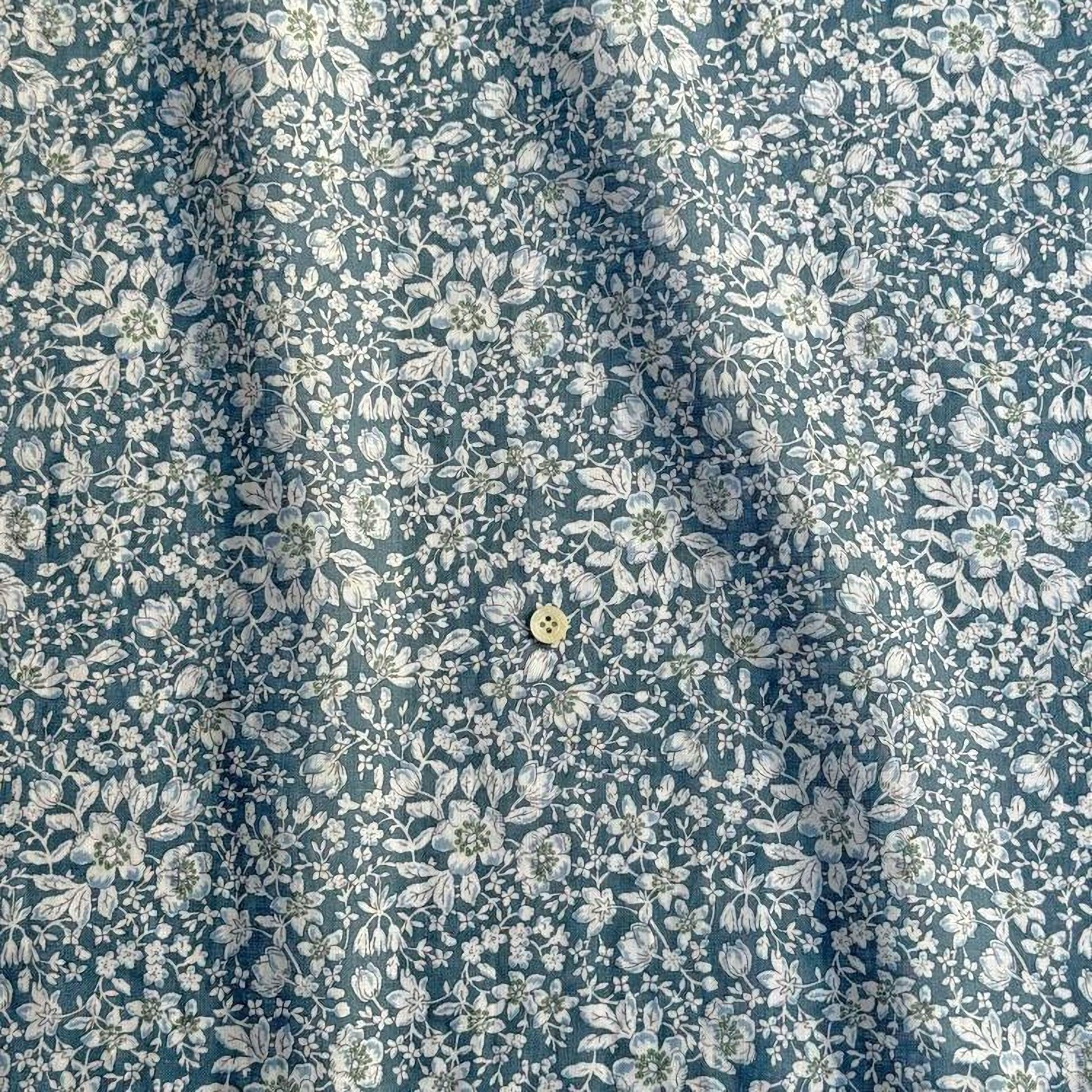 a close-up view of a fabric with a floral pattern in shades of blue and white. The fabric appears to be made of a material with a subtle texture, and there is a small button visible in the center of the fabric.