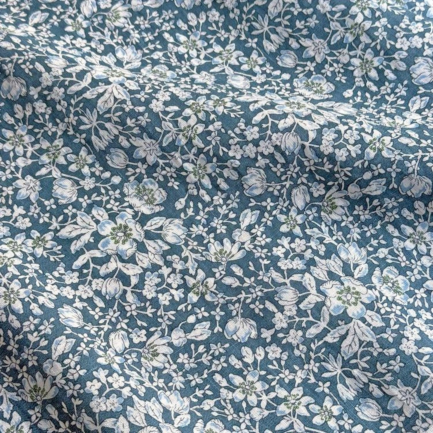 a close-up view of a fabric with a floral pattern in shades of blue and white. The pattern consists of various flowers and leaves, creating a visually appealing and intricate design.