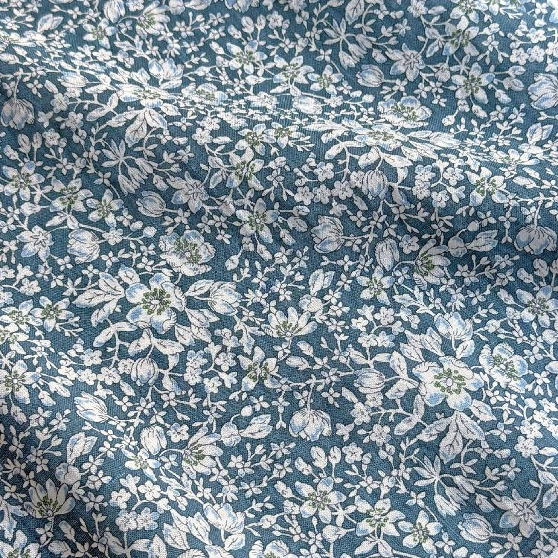 a close-up view of a fabric with a floral pattern in shades of blue and white. The pattern consists of various flowers and leaves, creating a visually appealing and intricate design.
