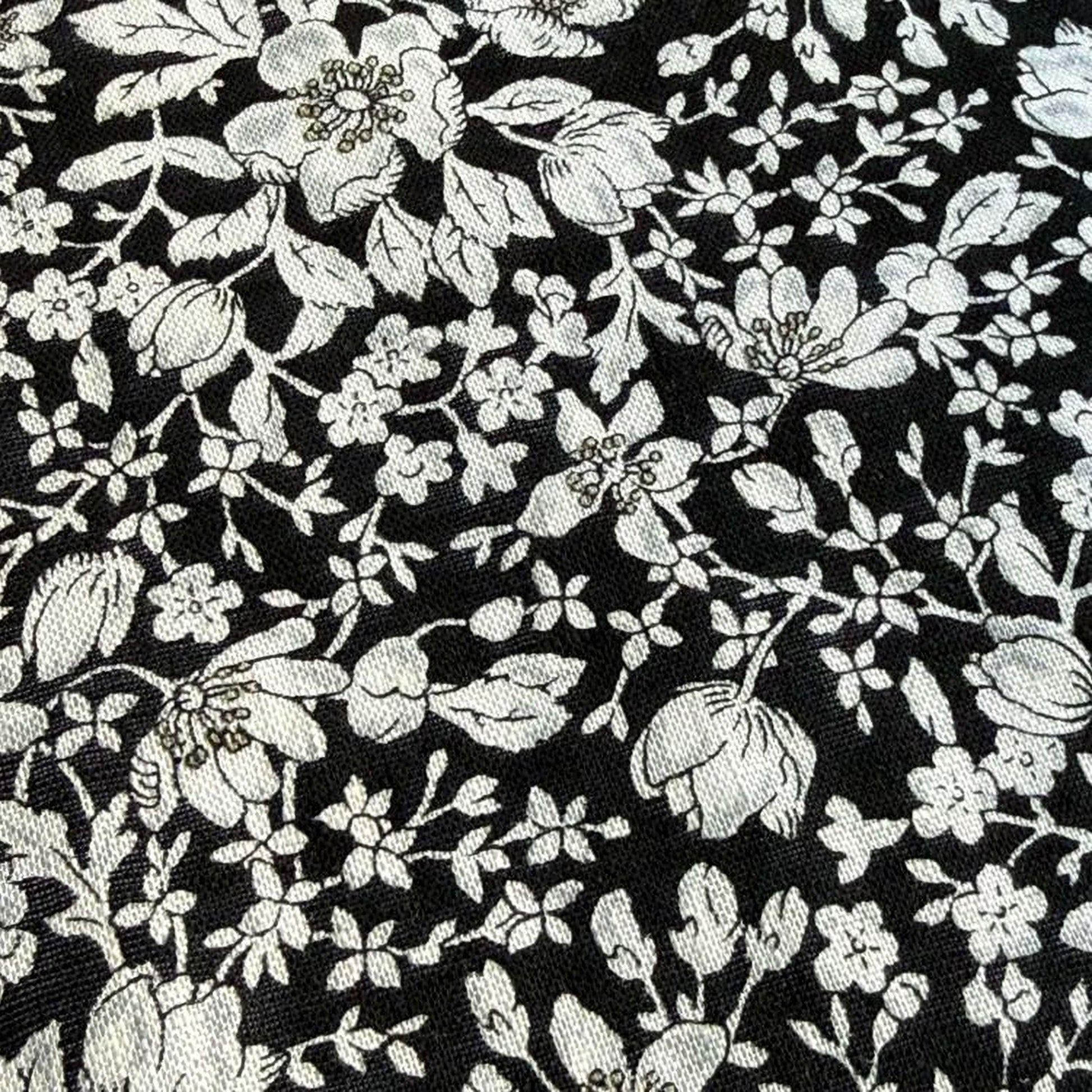 The image is a close-up of a black and white floral pattern, featuring numerous white flowers and leaves against a dark background.