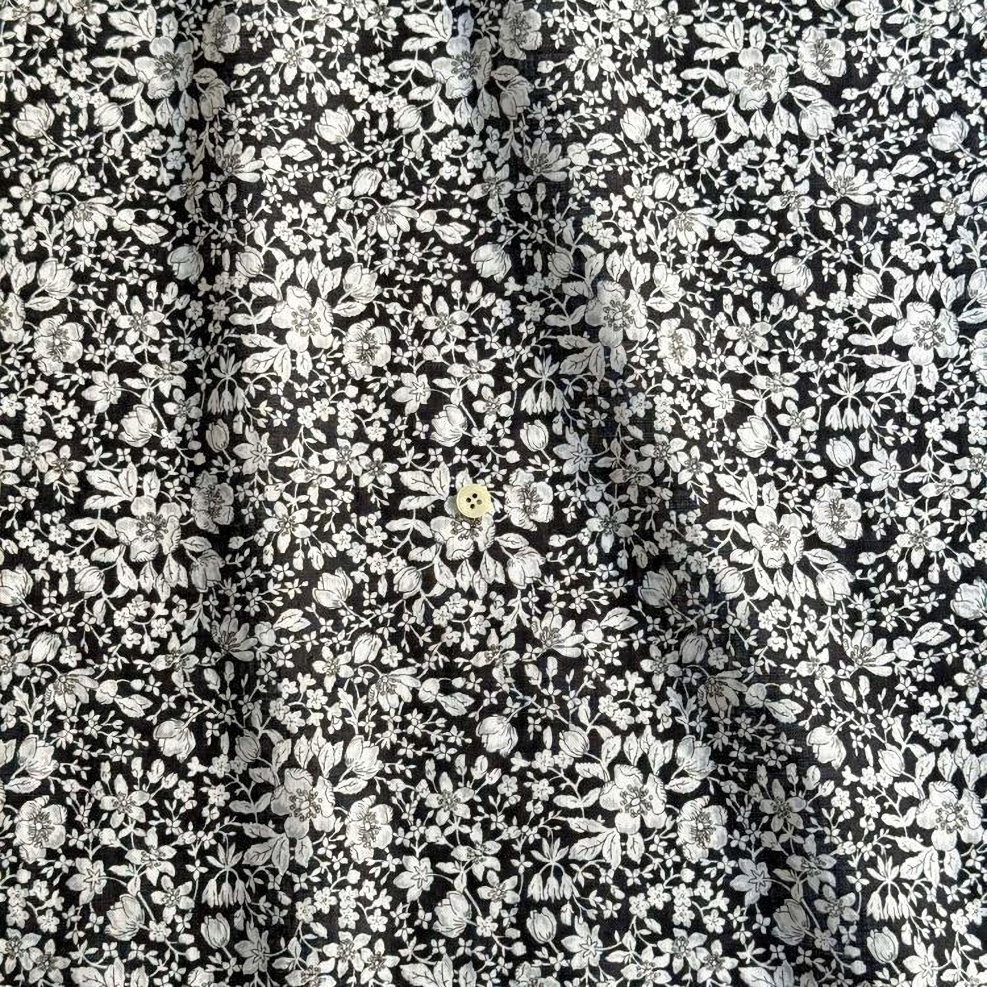 The image is a close-up of a fabric with a black and white floral pattern. The fabric appears to be made of a material with a floral design, possibly cotton or linen. The pattern consists of numerous small white flowers and leaves arranged in a repeating design across the fabric's surface. The image does not contain any text or other discernible objects or actions.