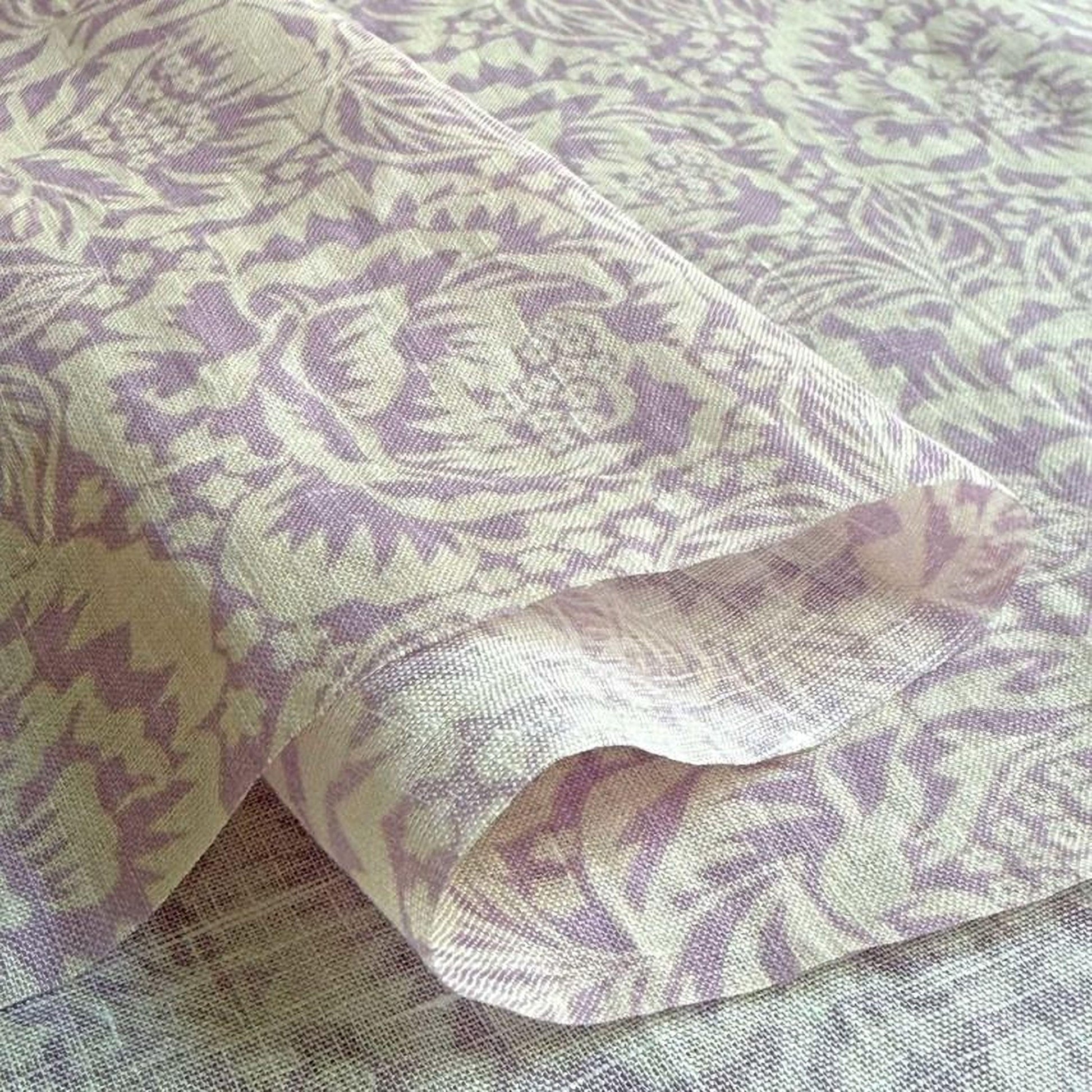 a close-up view of a fabric with a floral pattern in shades of purple and white. The fabric appears to be folded or rolled, revealing the intricate design and texture of the material.