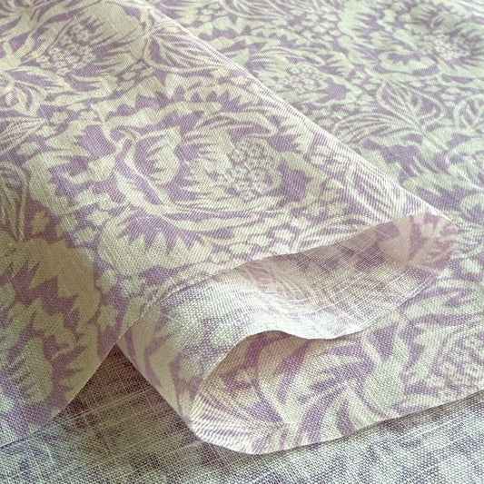 a close-up view of a fabric with a floral pattern in shades of purple and white. The fabric appears to be folded or rolled, revealing the intricate design and texture of the material.