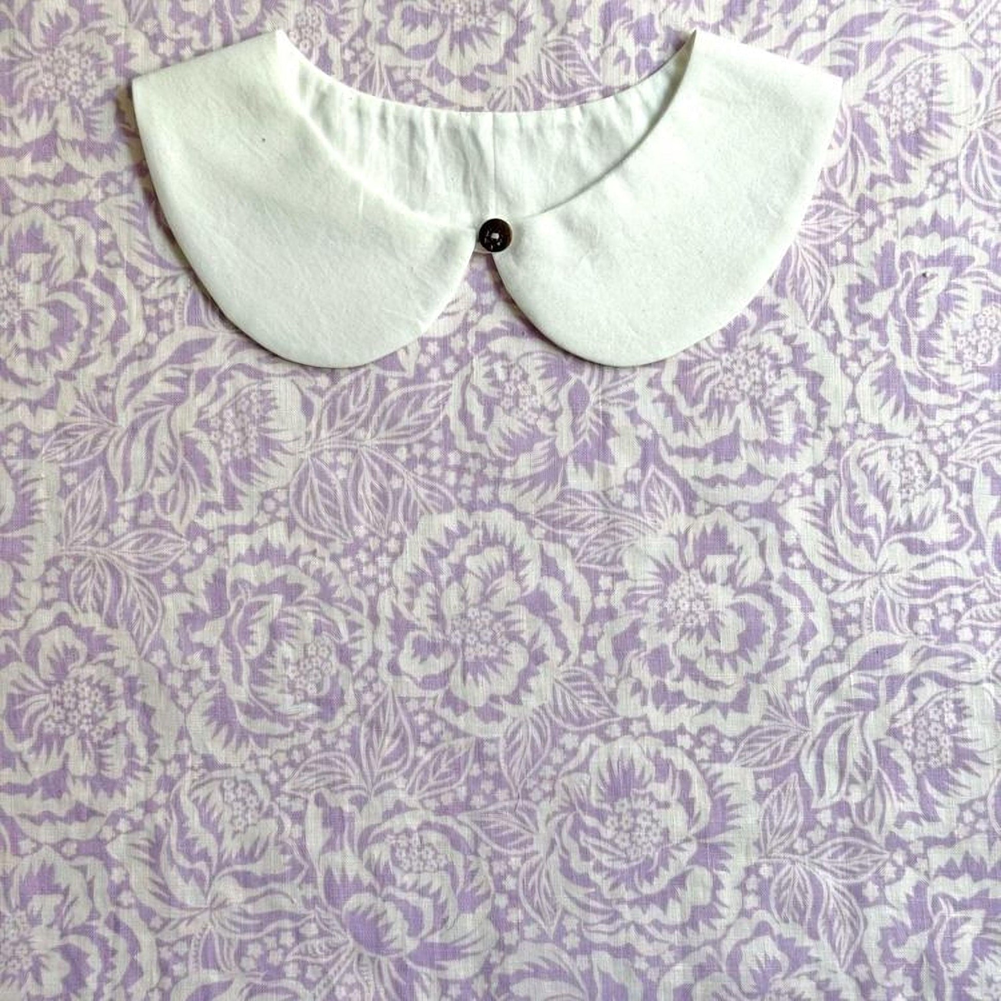 A white collar with a button is displayed against a background of a purple floral pattern.