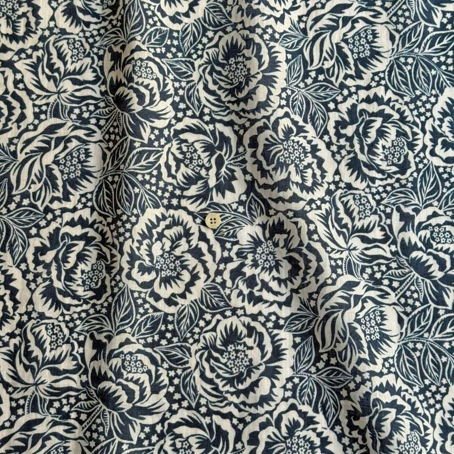 a close-up view of a fabric with a black and white floral pattern. The pattern consists of numerous flowers and leaves, creating a visually striking and intricate design. The fabric appears to be made of a soft, textured material, which adds to its overall aesthetic appeal.