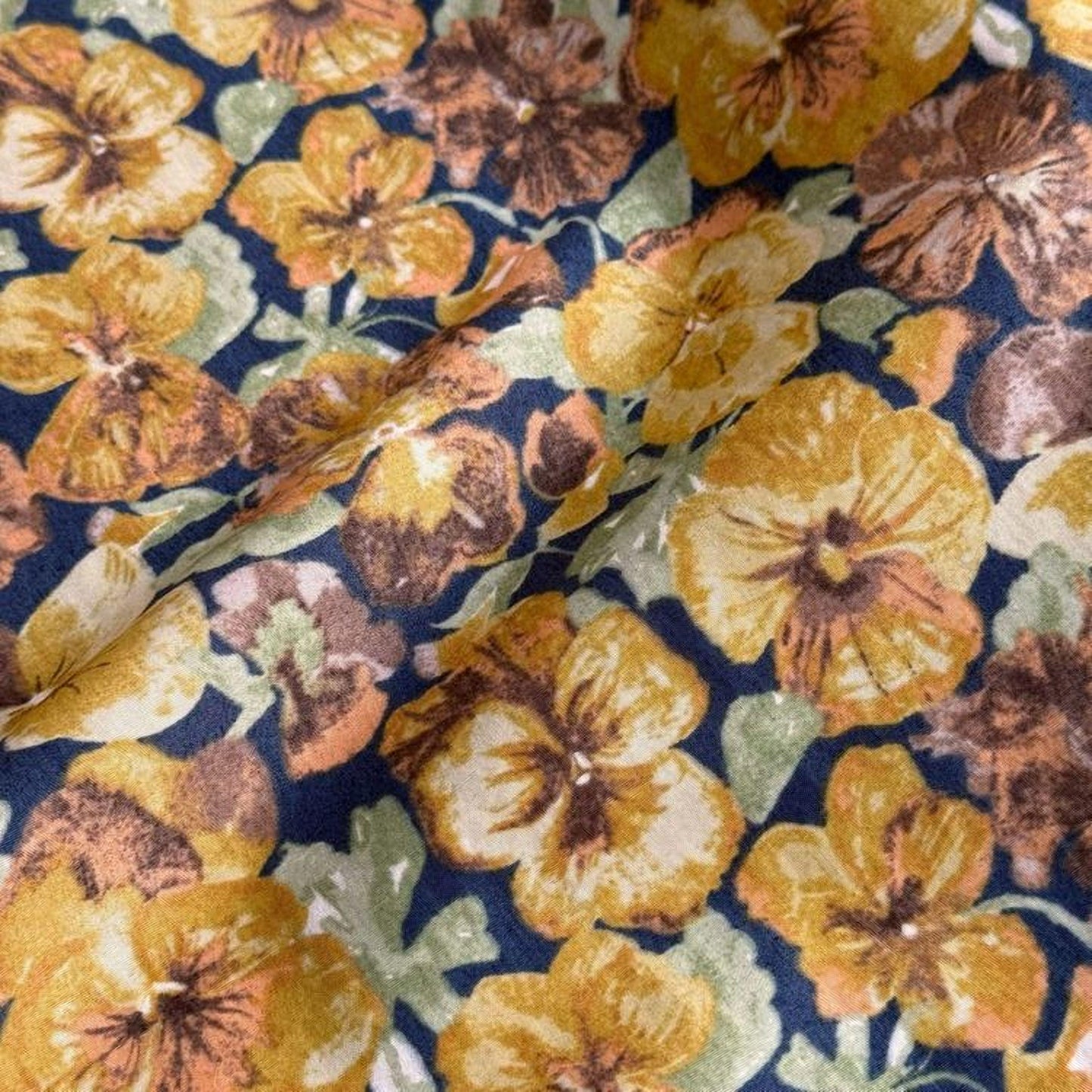 a close-up view of a fabric with a vibrant floral pattern featuring yellow and brown flowers against a dark blue background.
