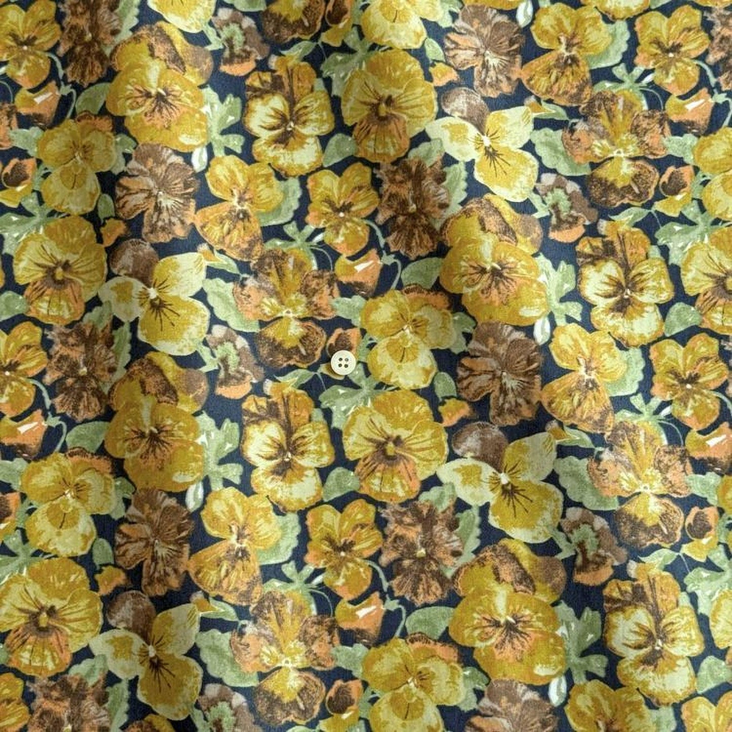 a close-up view of a fabric with a vibrant floral pattern of yellow and brown flowers, including pansies and daisies, against a dark background.