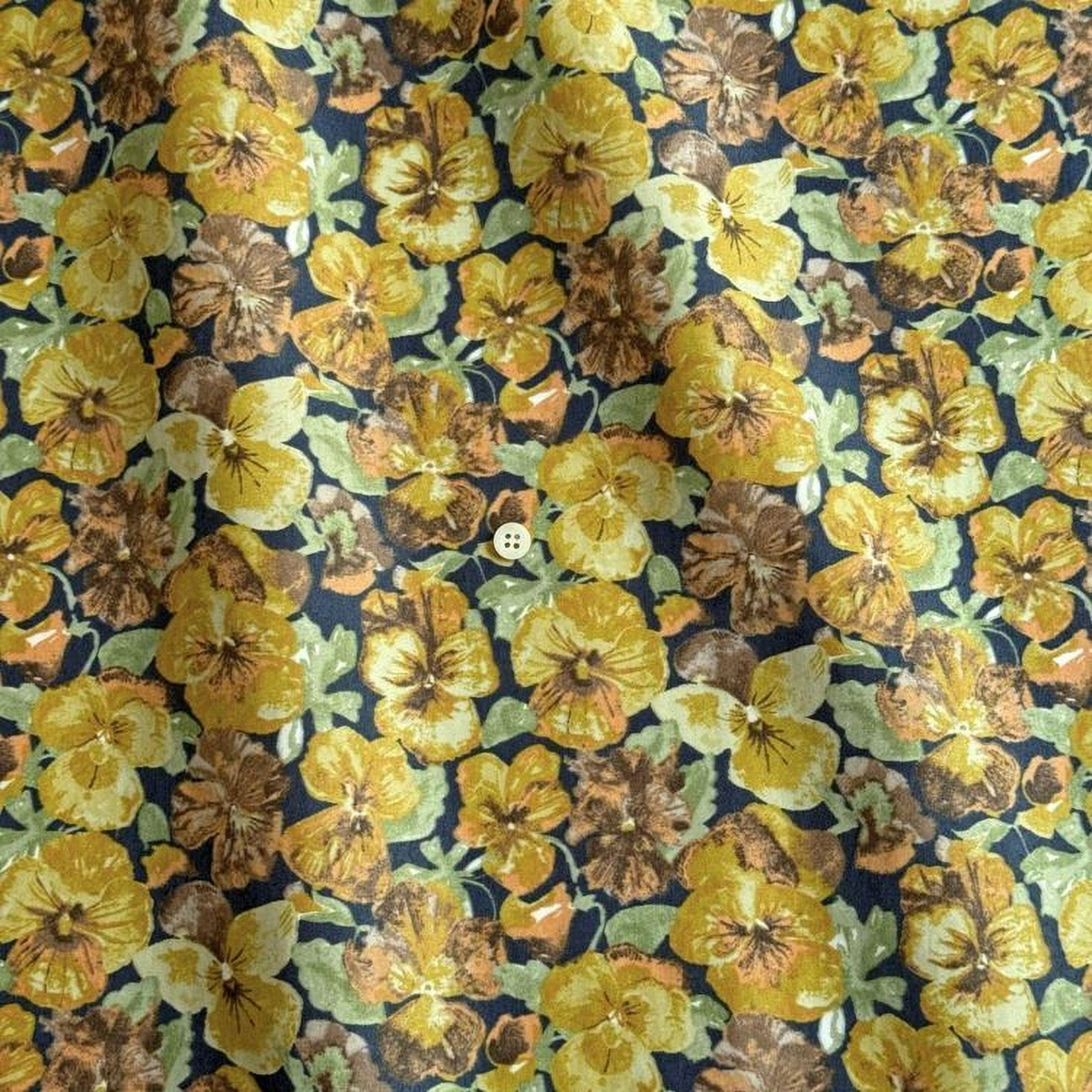 a close-up view of a fabric with a vibrant floral pattern of yellow and brown flowers, including pansies and daisies, against a dark background.