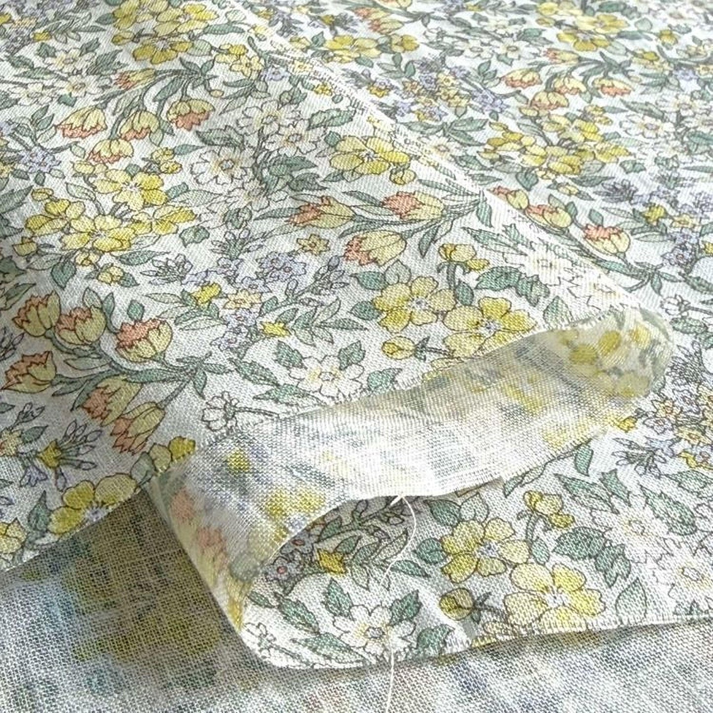 a close-up view of a fabric with a floral pattern, featuring yellow and green flowers and leaves. The fabric appears to be made of a soft, textured material, possibly cotton or linen.