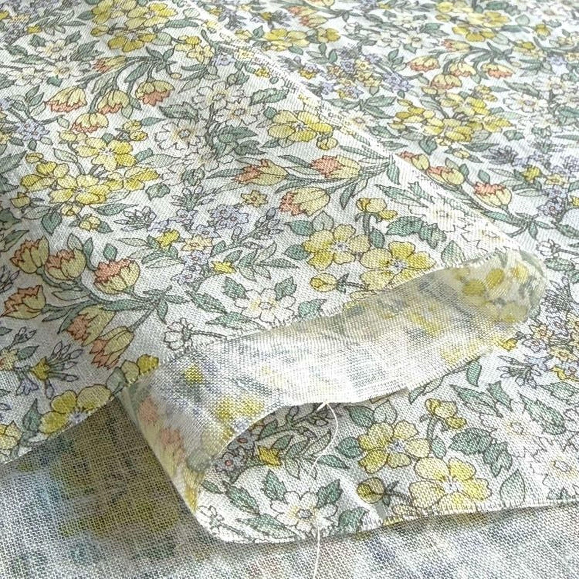 a close-up view of a fabric with a floral pattern, featuring yellow and green flowers and leaves. The fabric appears to be made of a soft, textured material, possibly cotton or linen.