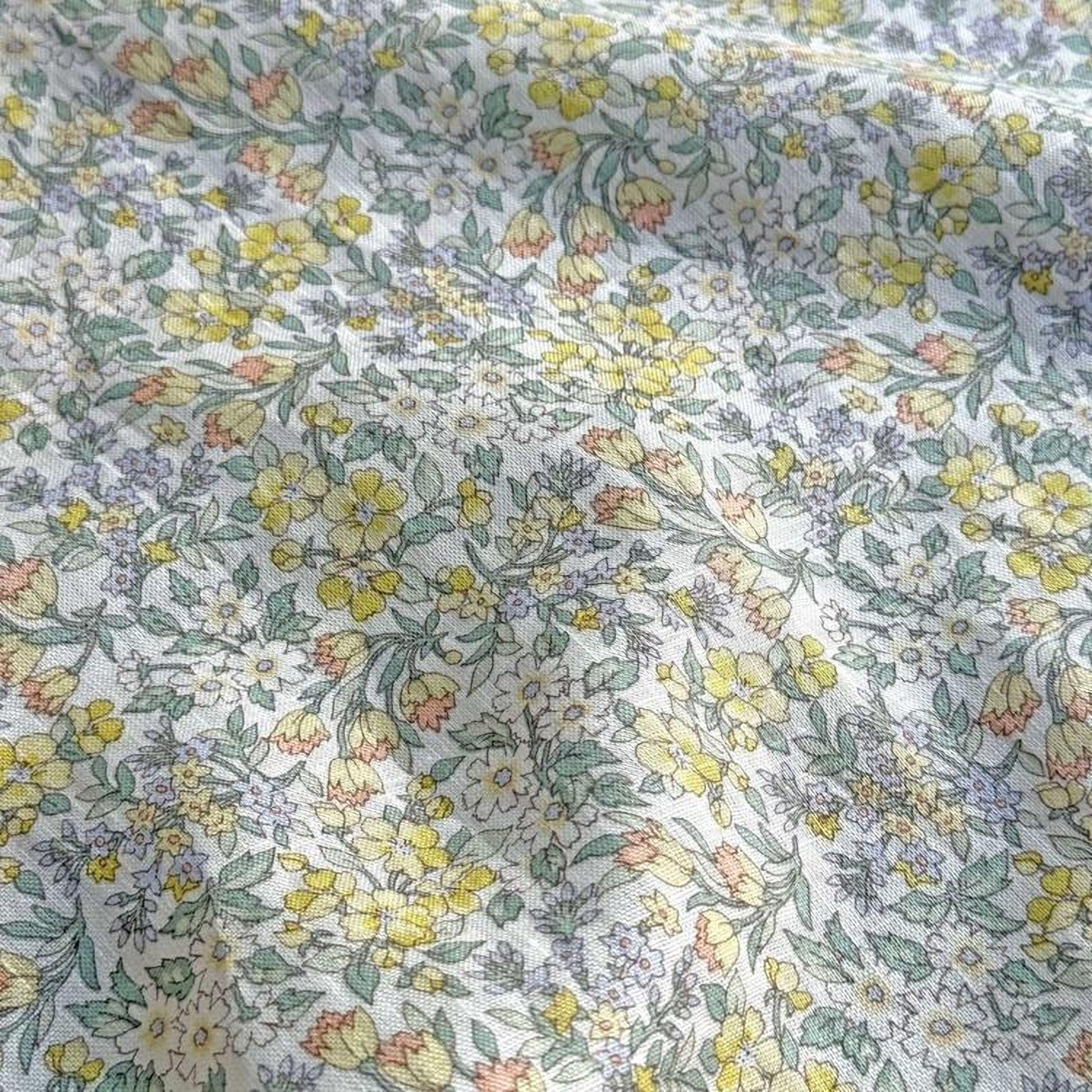 a close-up view of a fabric with a floral pattern, featuring a variety of yellow and green flowers and leaves.