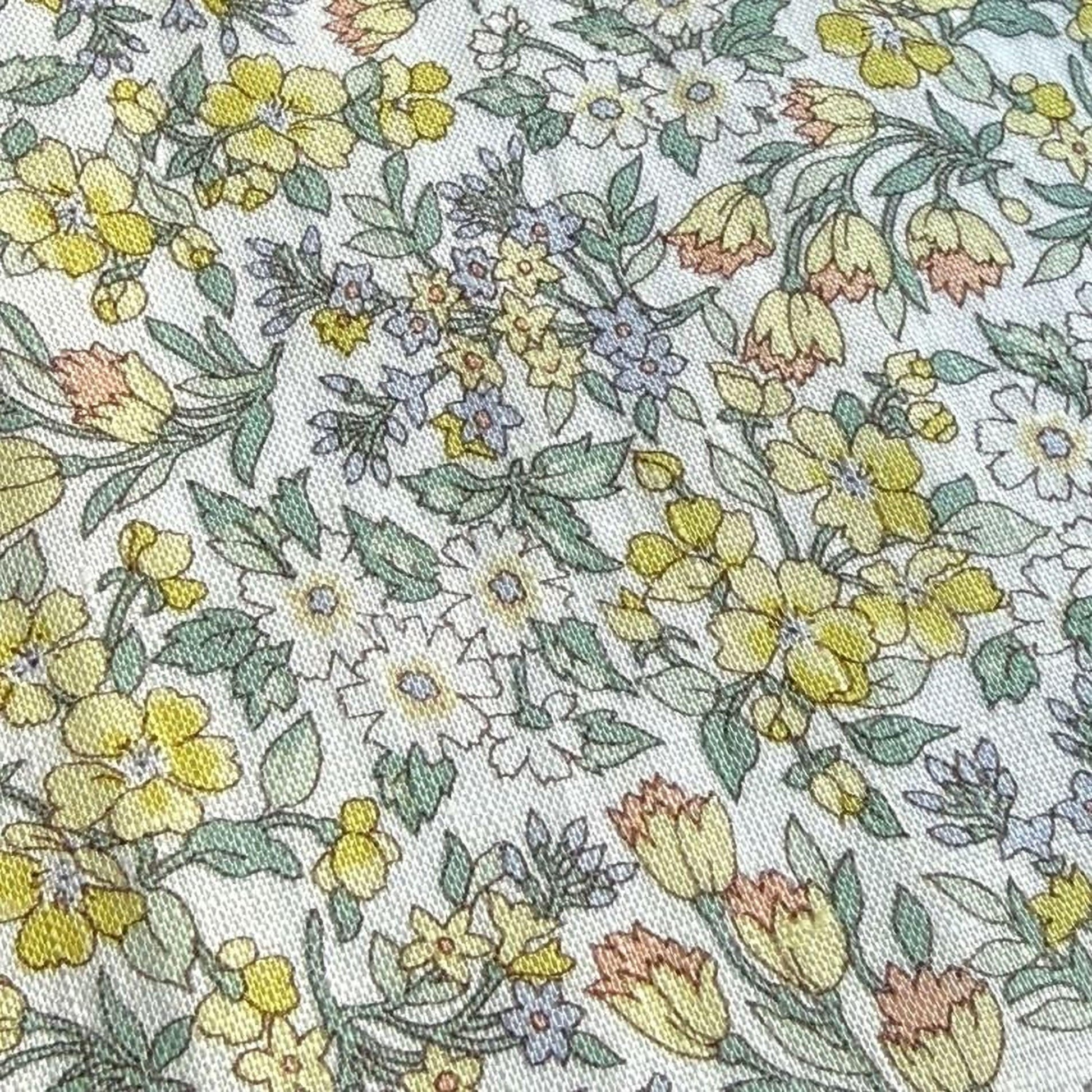a close-up view of a fabric with a floral pattern. The pattern consists of various flowers and leaves in shades of yellow, green, and white, creating a vibrant and colorful design.