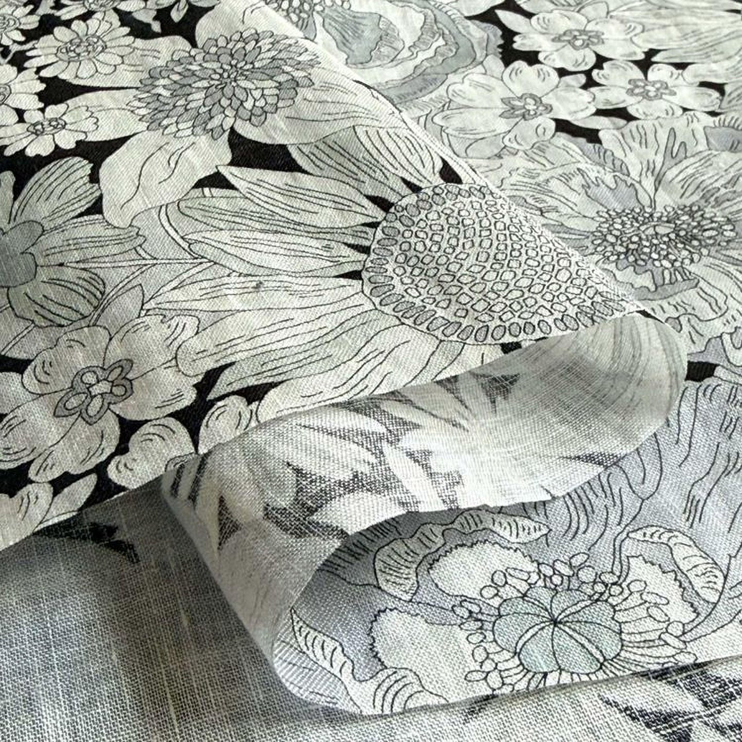 a close-up view of a fabric with a floral pattern, including various types of flowers and leaves. The fabric appears to be made of a soft, textured material, possibly cotton or linen. The image does not contain any text or other discernible objects or actions.