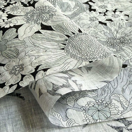 a close-up view of a fabric with a floral pattern, including various types of flowers and leaves. The fabric appears to be made of a soft, textured material, possibly cotton or linen. The image does not contain any text or other discernible objects or actions.