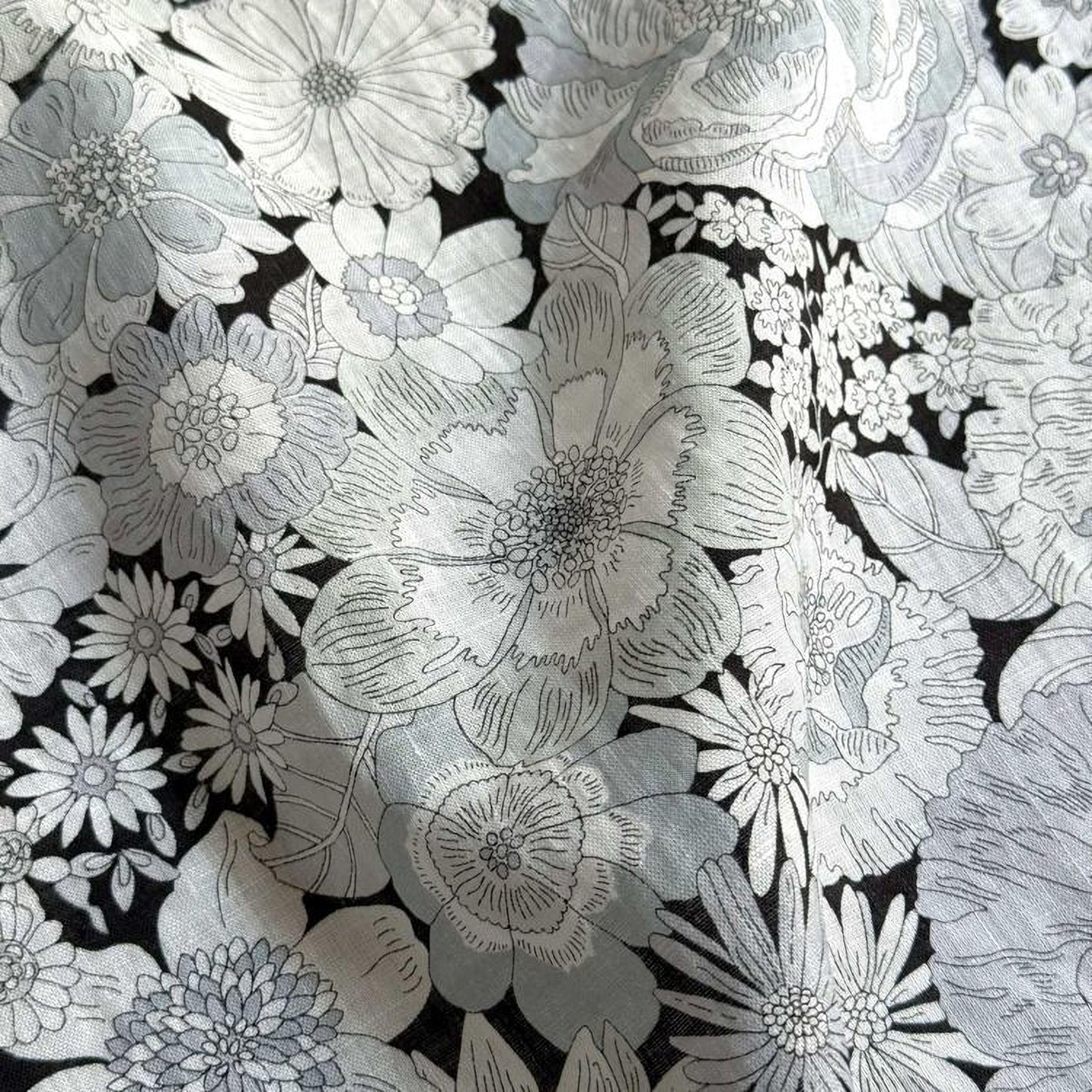 The image is a close-up of a fabric with a repeating pattern of white and gray flowers and leaves. The pattern is intricate and detailed, with various sizes and shapes of flowers and leaves filling the entire fabric. The image does not contain any text or other objects, and the focus is solely on the floral pattern.