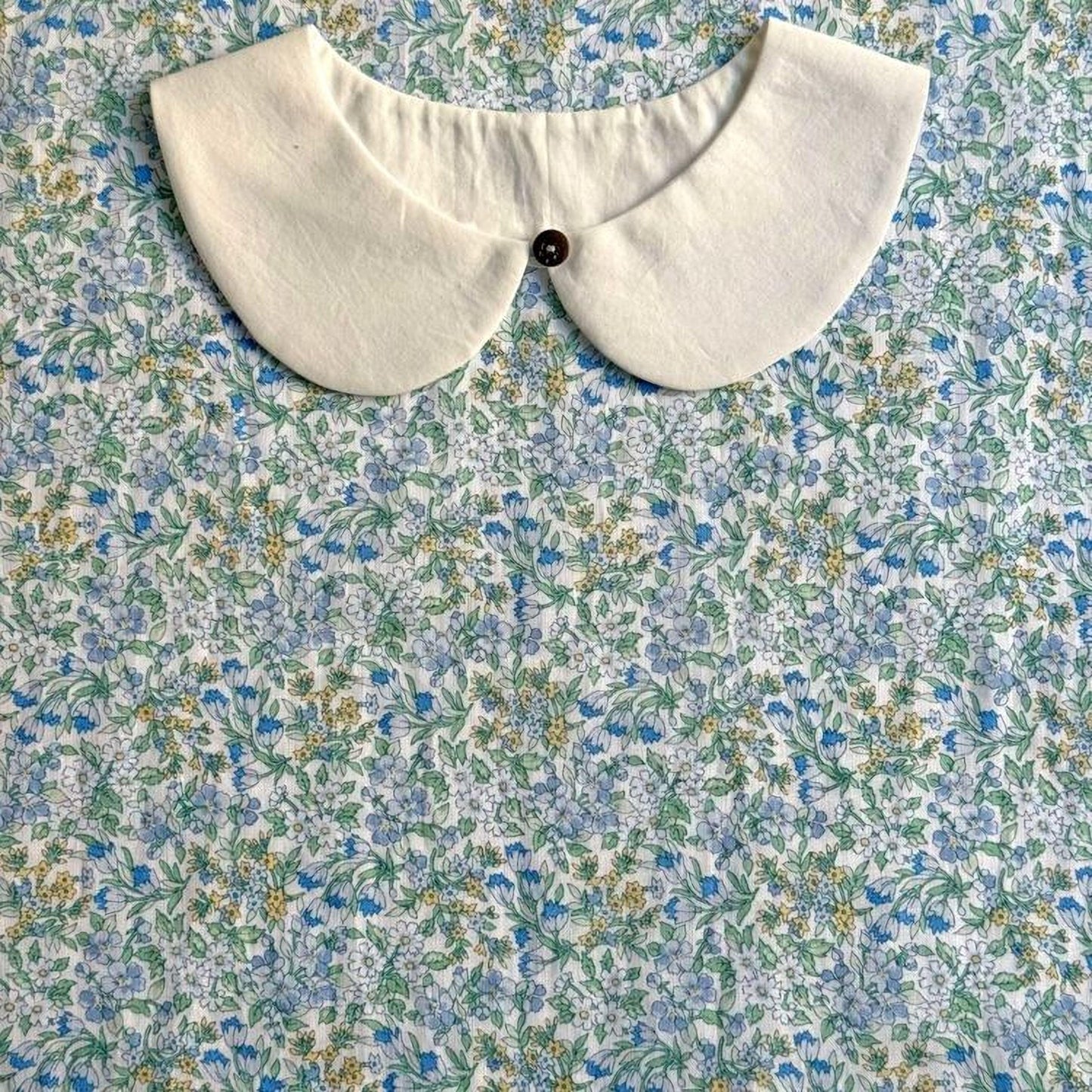 a white collar with a button, placed on a fabric with a floral pattern.
