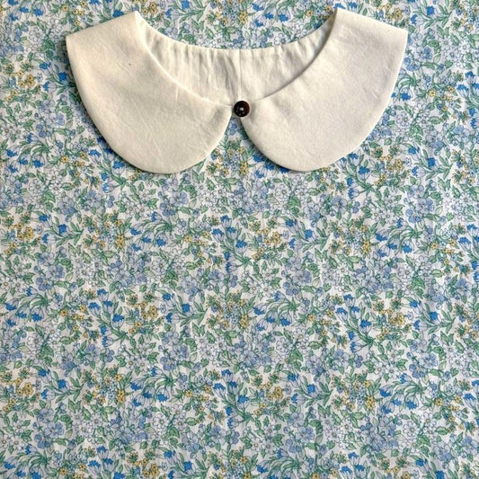 a white collar with a button, placed on a fabric with a floral pattern.
