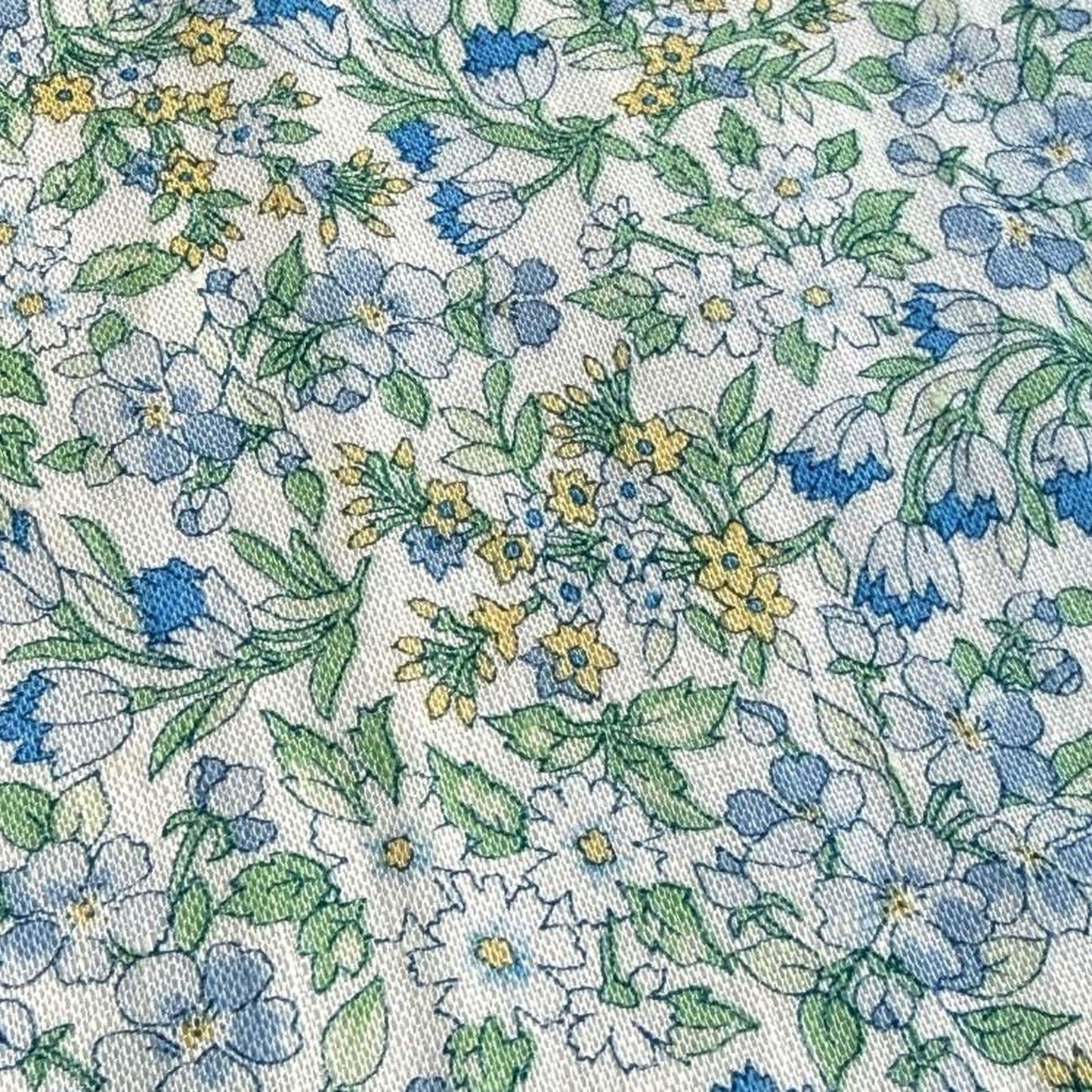 a close-up view of a fabric with a floral pattern. The pattern consists of various flowers and leaves in shades of blue, green, and yellow, creating a vibrant and colorful design. The fabric appears to be a textile or material with a printed pattern, showcasing the intricate details and textures of the floral design.