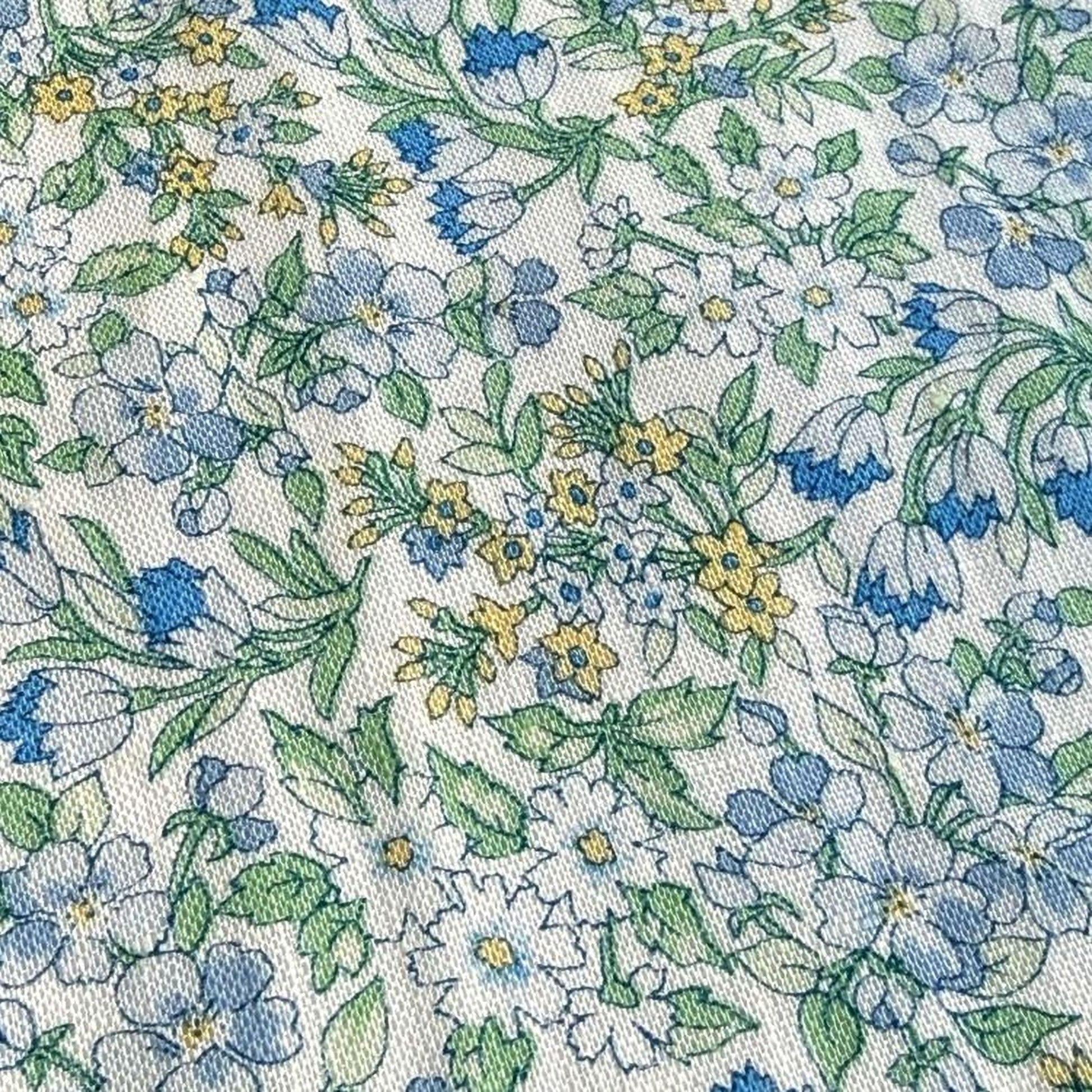 a close-up view of a fabric with a floral pattern. The pattern consists of various flowers and leaves in shades of blue, green, and yellow, creating a vibrant and colorful design. The fabric appears to be a textile or material with a printed pattern, showcasing the intricate details and textures of the floral design.