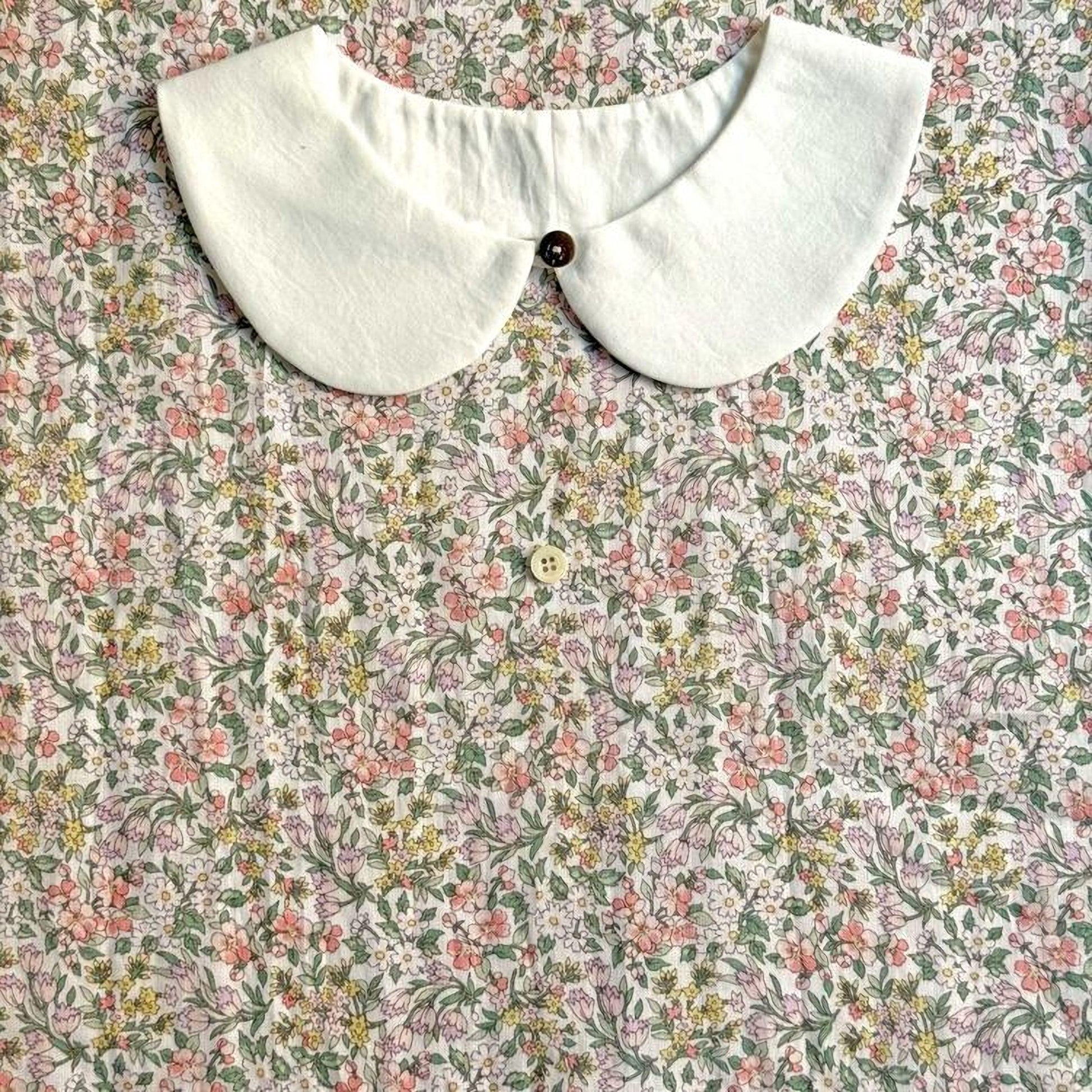 a white collar with a button, placed on a floral print fabric.