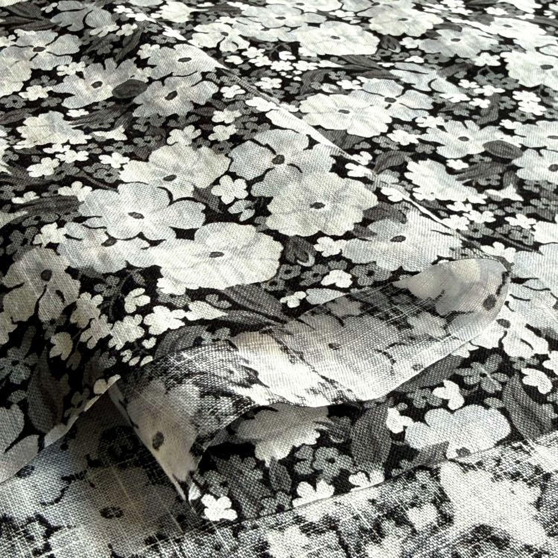 a close-up view of a fabric with a black and white floral pattern. The fabric appears to be a piece of clothing or textile, with the pattern consisting of numerous small white flowers arranged in a repeating design. The image does not contain any text or other discernible objects, and the focus is solely on the floral pattern.