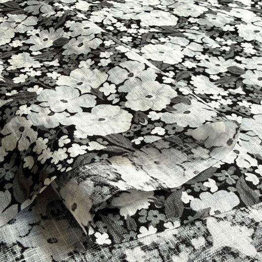 a close-up view of a fabric with a black and white floral pattern. The fabric appears to be a piece of clothing or textile, with the pattern consisting of numerous small white flowers arranged in a repeating design. The image does not contain any text or other discernible objects, and the focus is solely on the floral pattern.