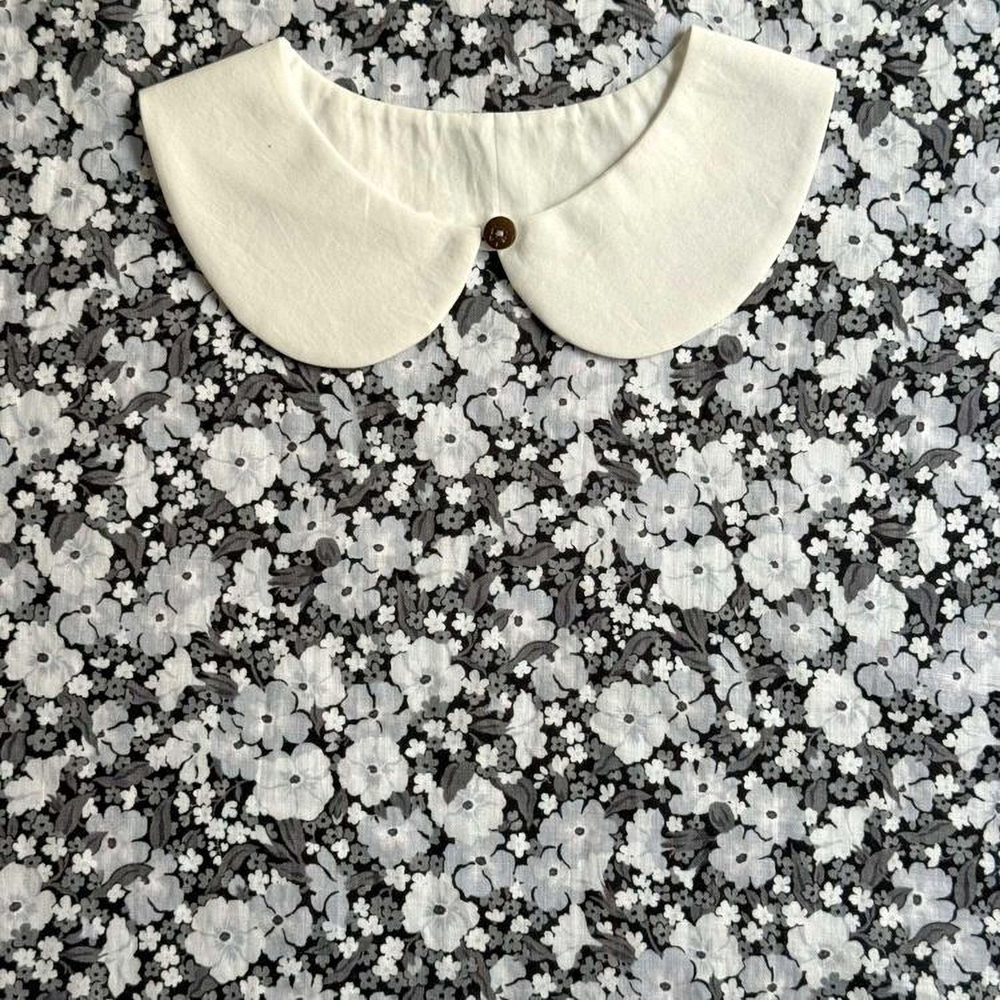 A white collar is displayed against a background of a black and white floral pattern.