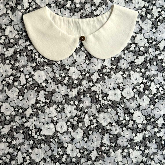A white collar is displayed against a background of a black and white floral pattern.