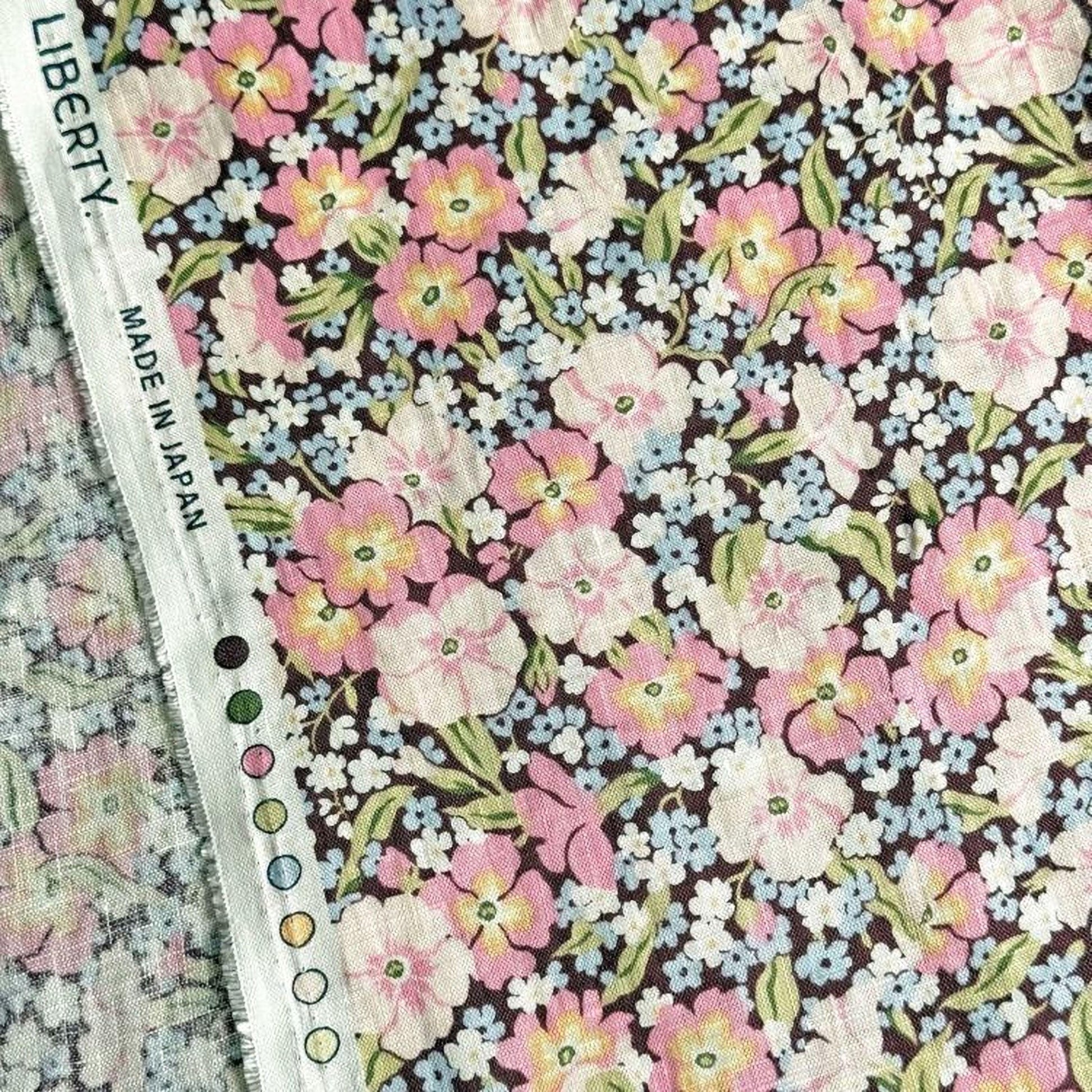 a close-up view of a fabric with a floral pattern, featuring a variety of pink, white, and blue flowers. The fabric appears to be made in Japan, as indicated by the text "LIBERTY. MADE IN JAPAN" visible on the fabric.