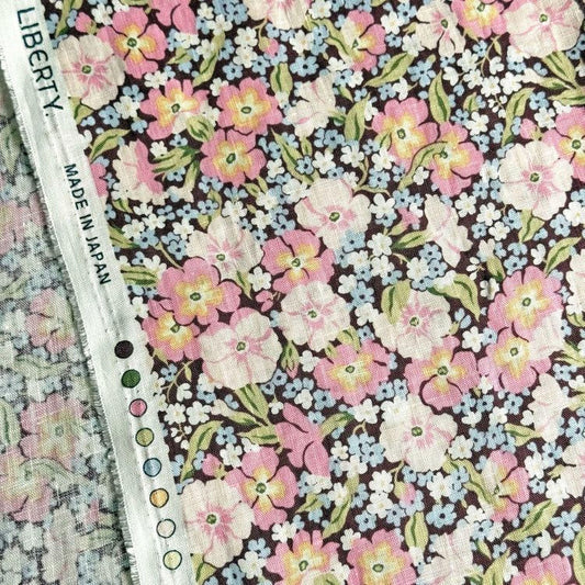 a close-up view of a fabric with a floral pattern, featuring a variety of pink, white, and blue flowers. The fabric appears to be made in Japan, as indicated by the text "LIBERTY. MADE IN JAPAN" visible on the fabric.