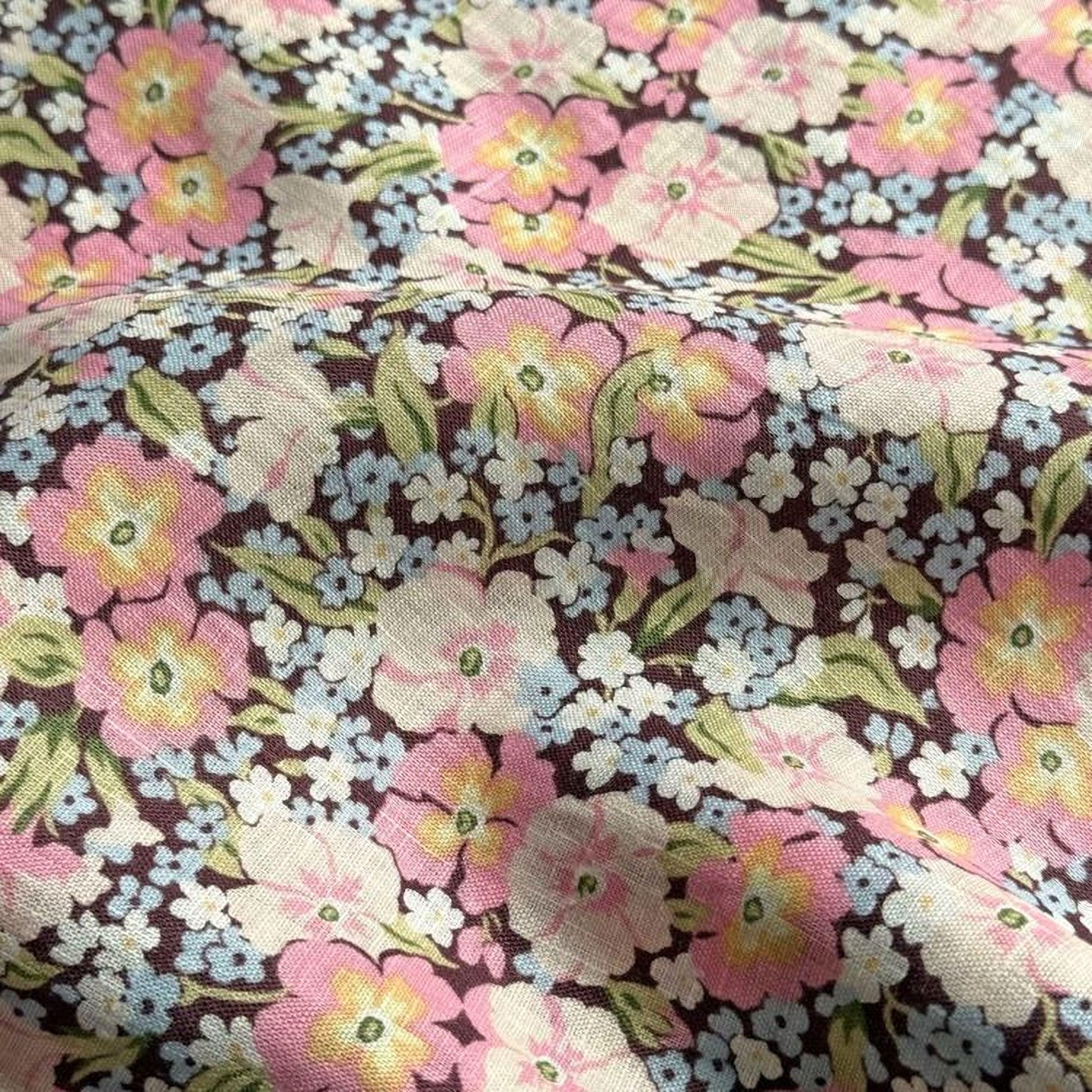 a close-up view of a fabric with a floral pattern. The fabric has a mix of pink, white, and yellow flowers, along with green leaves, creating a vibrant and colorful design.