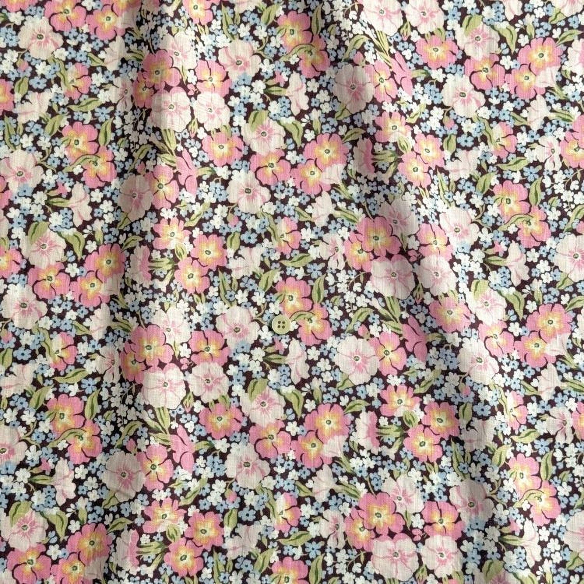 a close-up view of a fabric with a floral pattern. The fabric has a mix of pink, white, and blue flowers, along with green leaves, creating a vibrant and colorful design. The pattern repeats across the fabric, creating a visually appealing and eye-catching design.