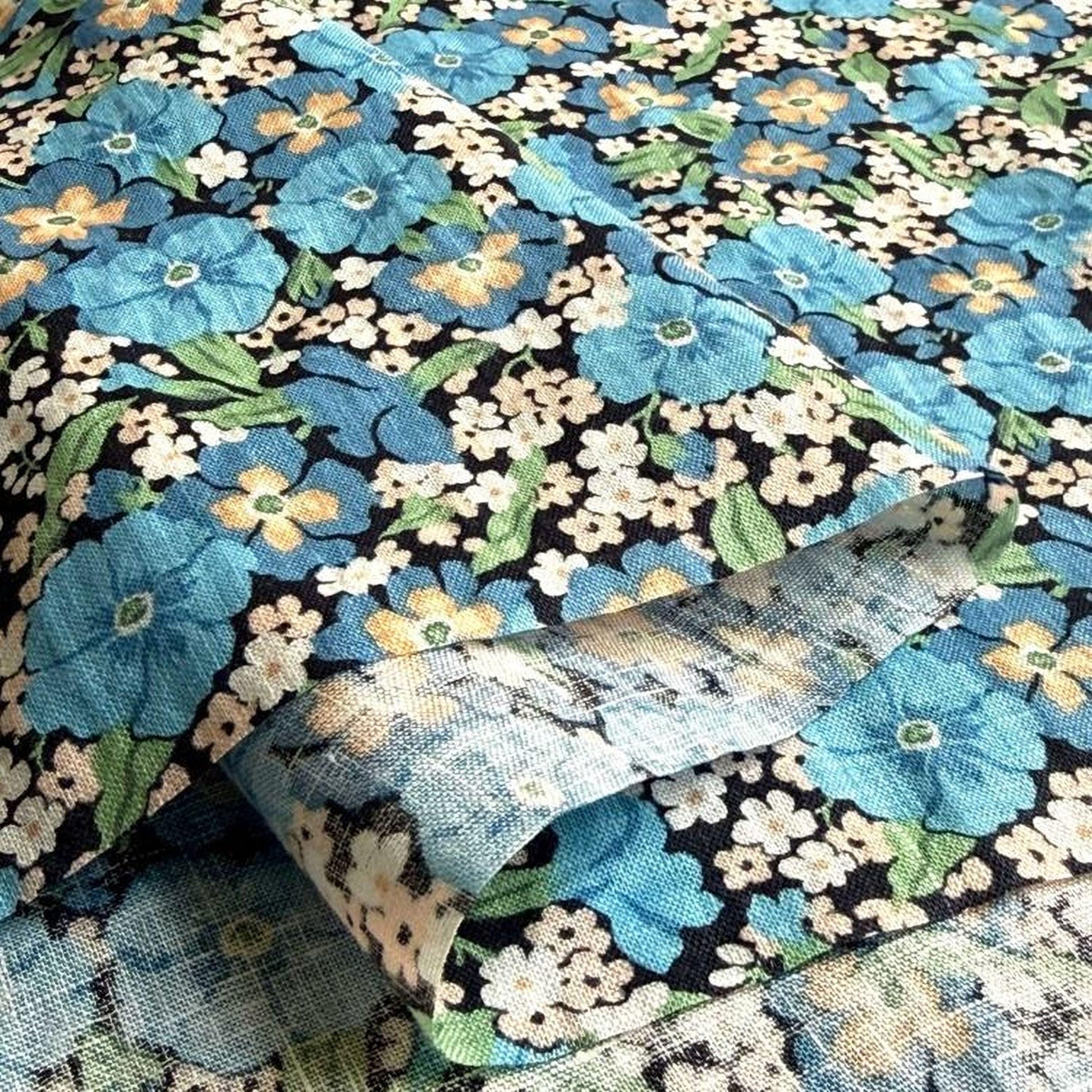 a close-up view of a fabric with a floral pattern in shades of blue, green, and white. The fabric appears to be folded or rolled, revealing the intricate design of the flowers and leaves.