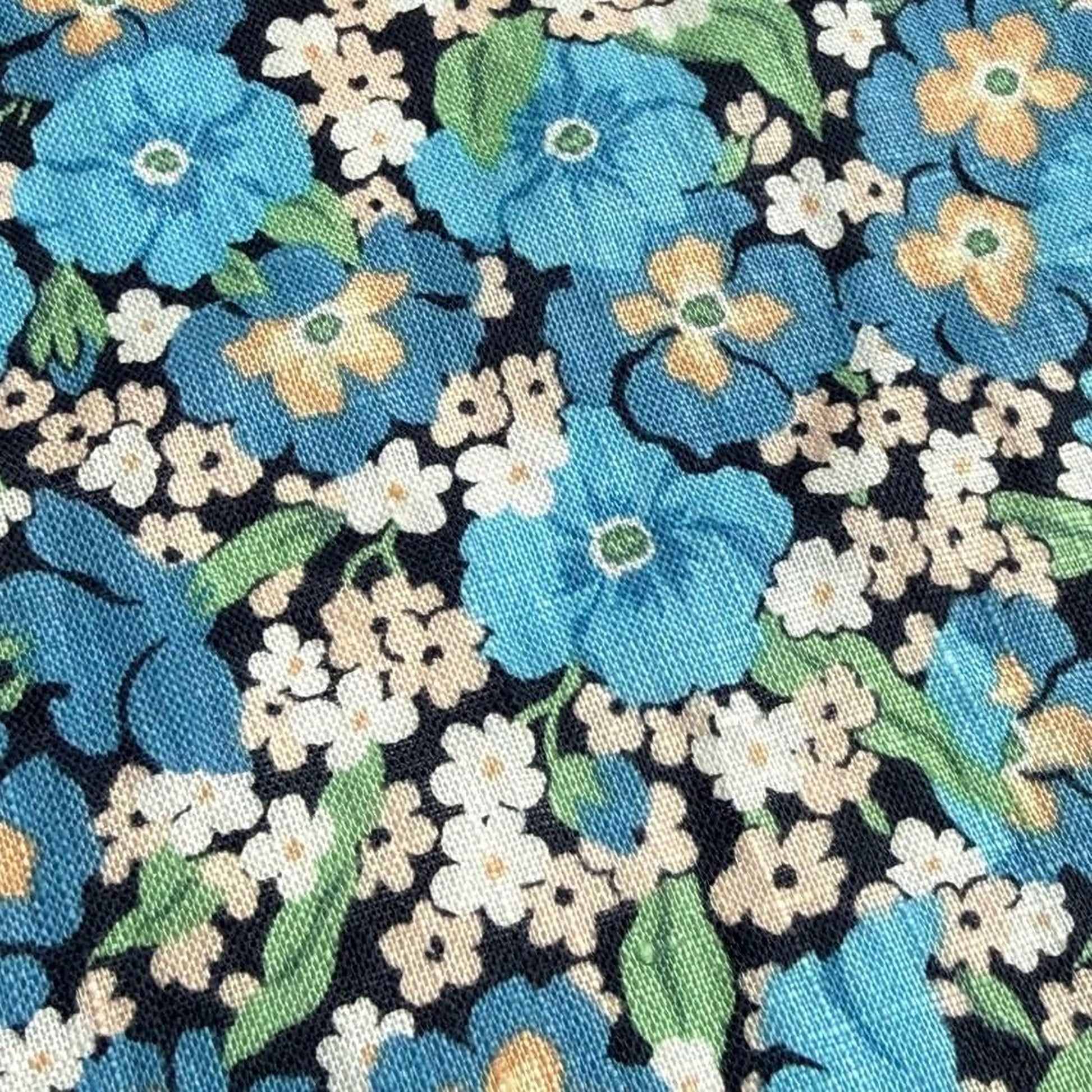 a close-up view of a fabric with a floral pattern. The fabric is predominantly blue and white, with various shades of blue and white flowers and leaves scattered across the fabric. The pattern is intricate and detailed, showcasing the craftsmanship of the fabric.