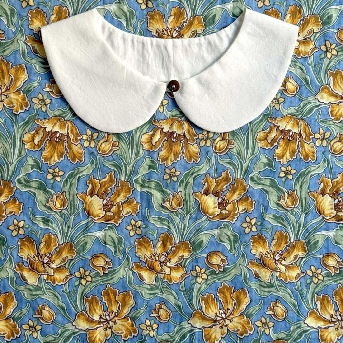 a white collar with a button, set against a blue floral print background.