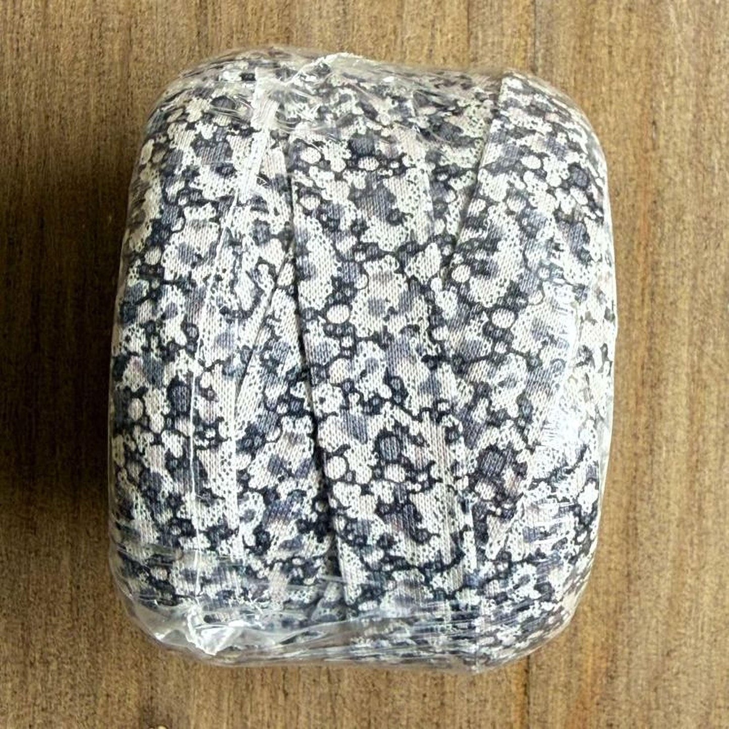 A square-shaped object with a black and white floral pattern, wrapped in plastic and placed on a wooden surface.