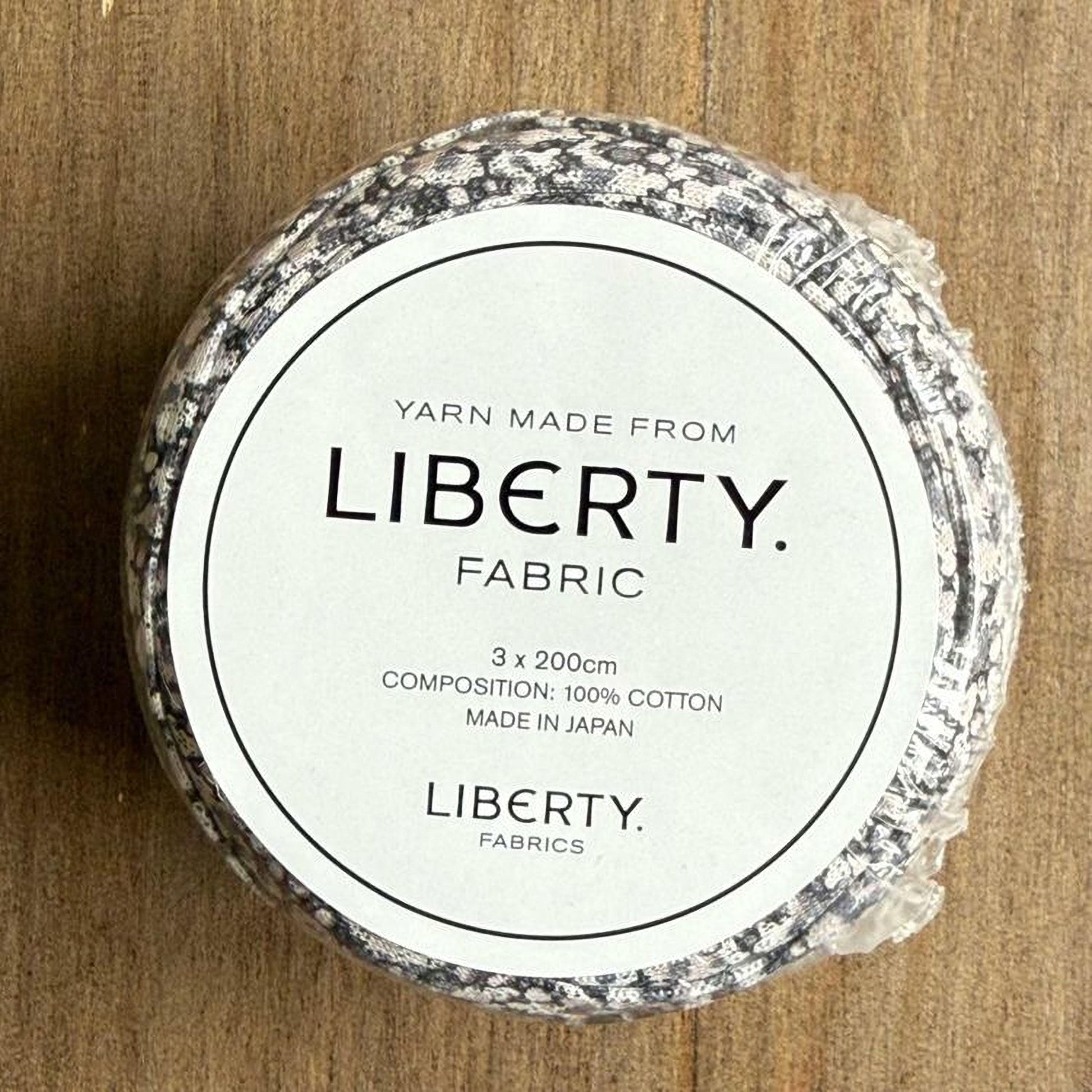 A white label with black text on a wooden surface, indicating that the yarn is made from Liberty fabric.