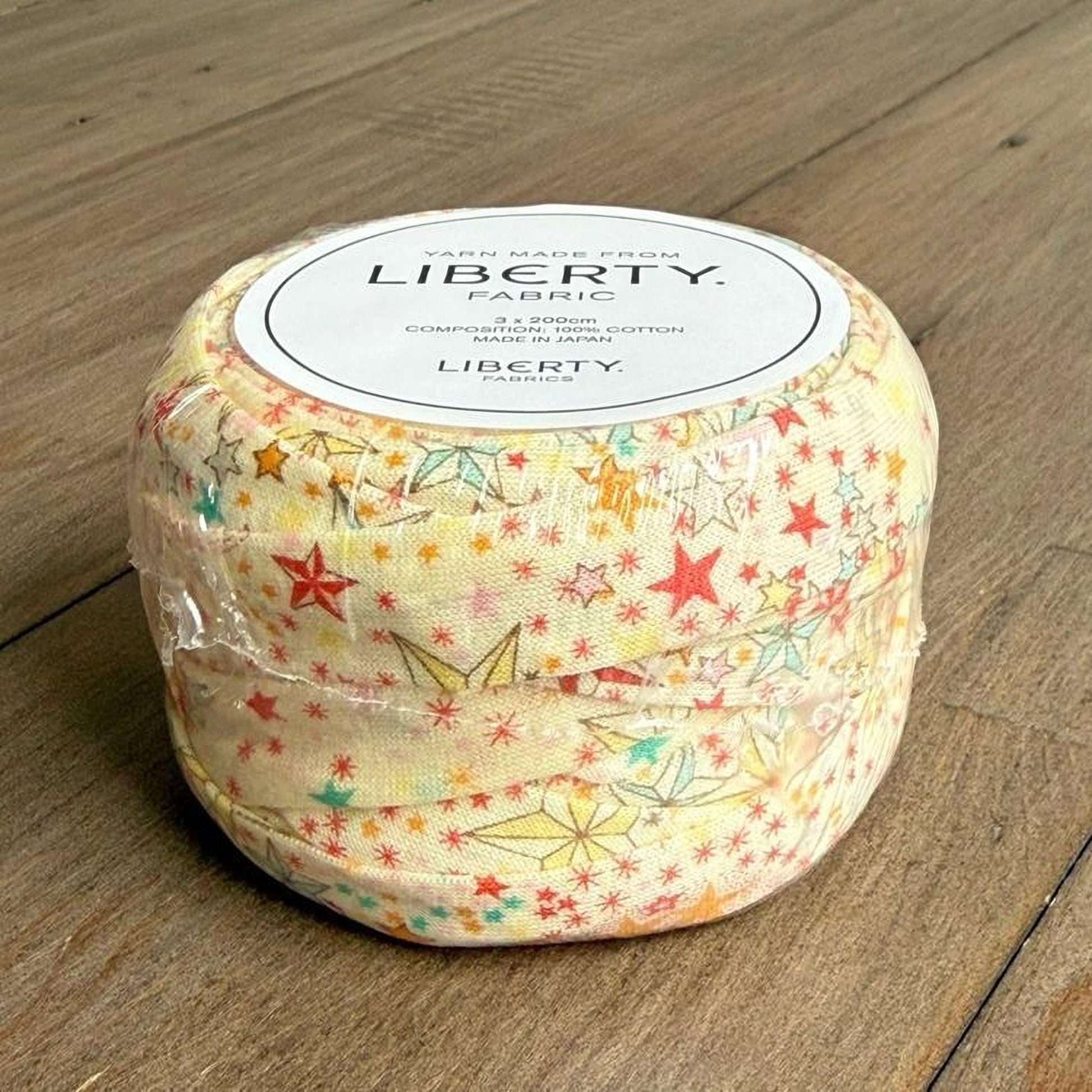 A package of fabric with a colorful star and flower pattern, sitting on a wooden surface.