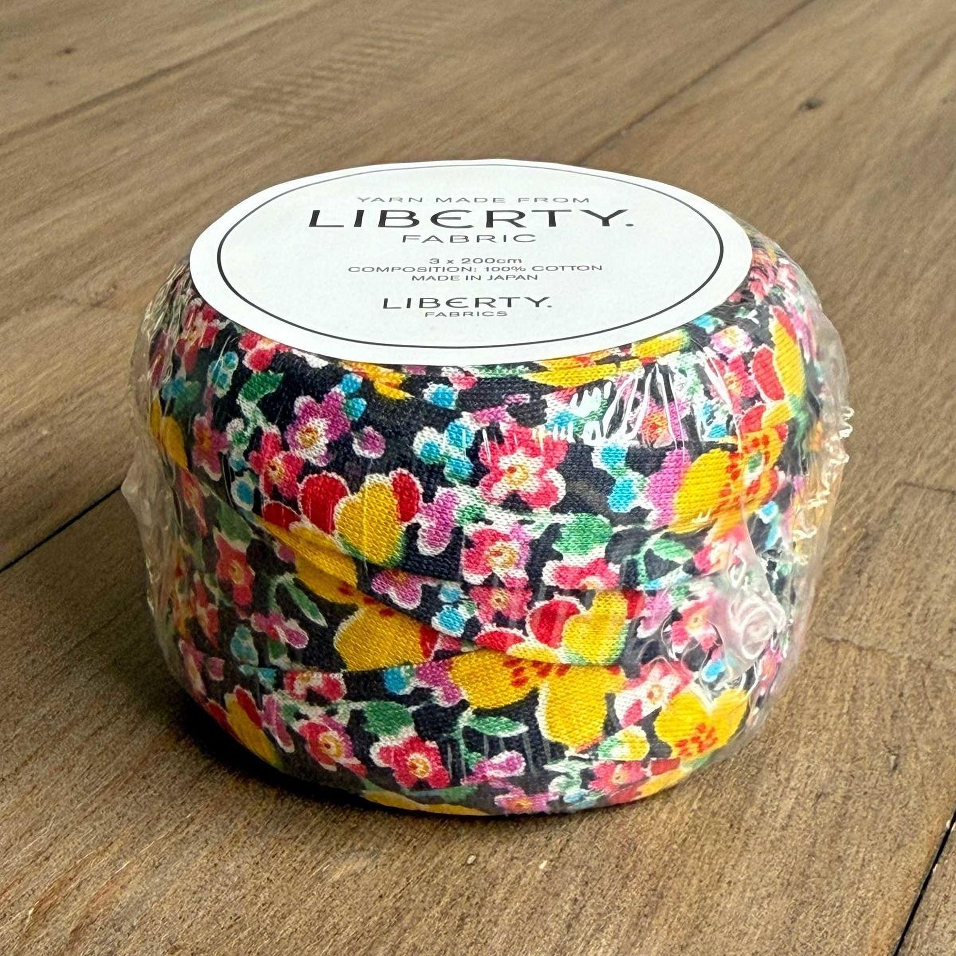 A package of Liberty fabric spools, featuring a vibrant floral pattern in shades of pink, yellow, and green.