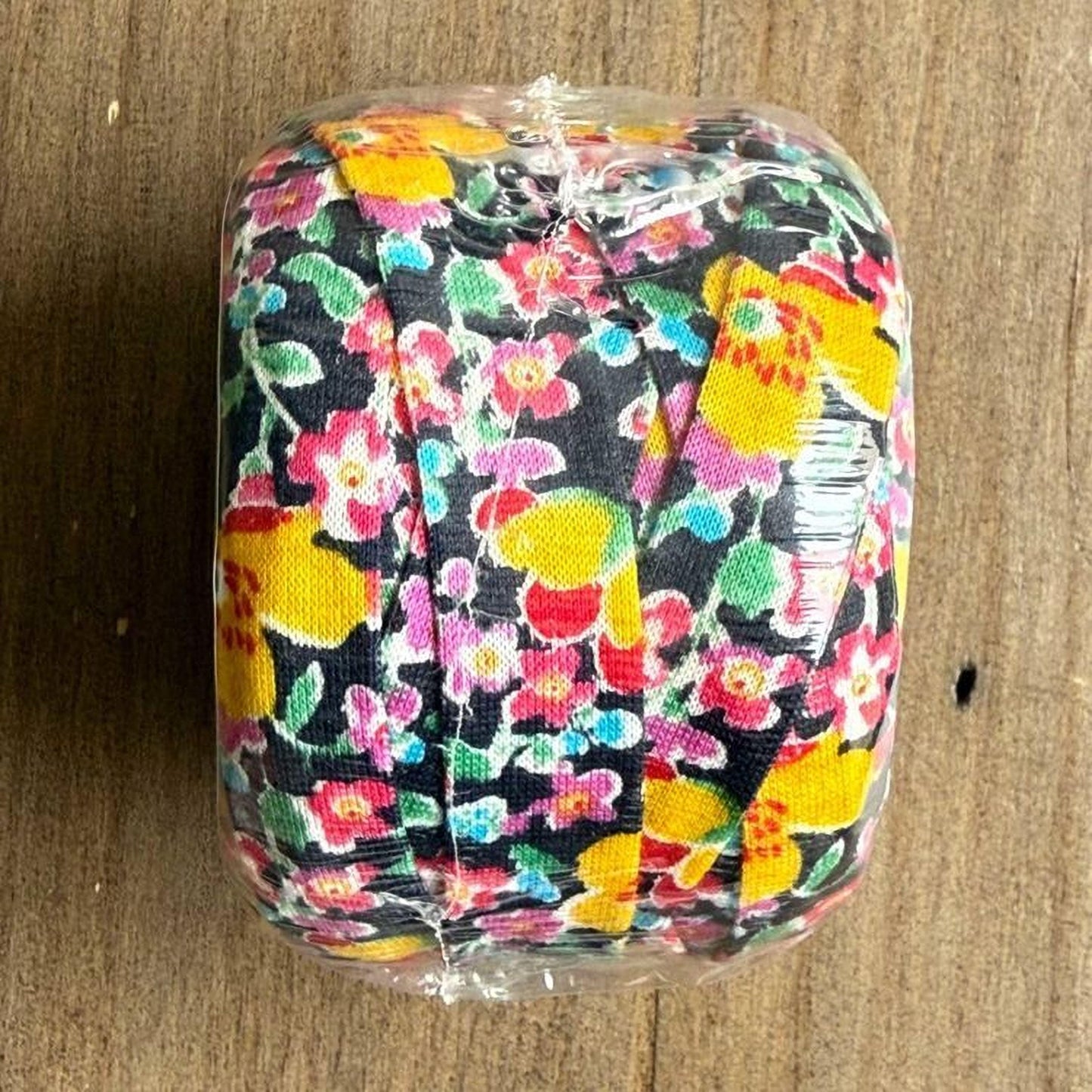 A roll of colorful floral fabric is wrapped in plastic and placed on a wooden surface.