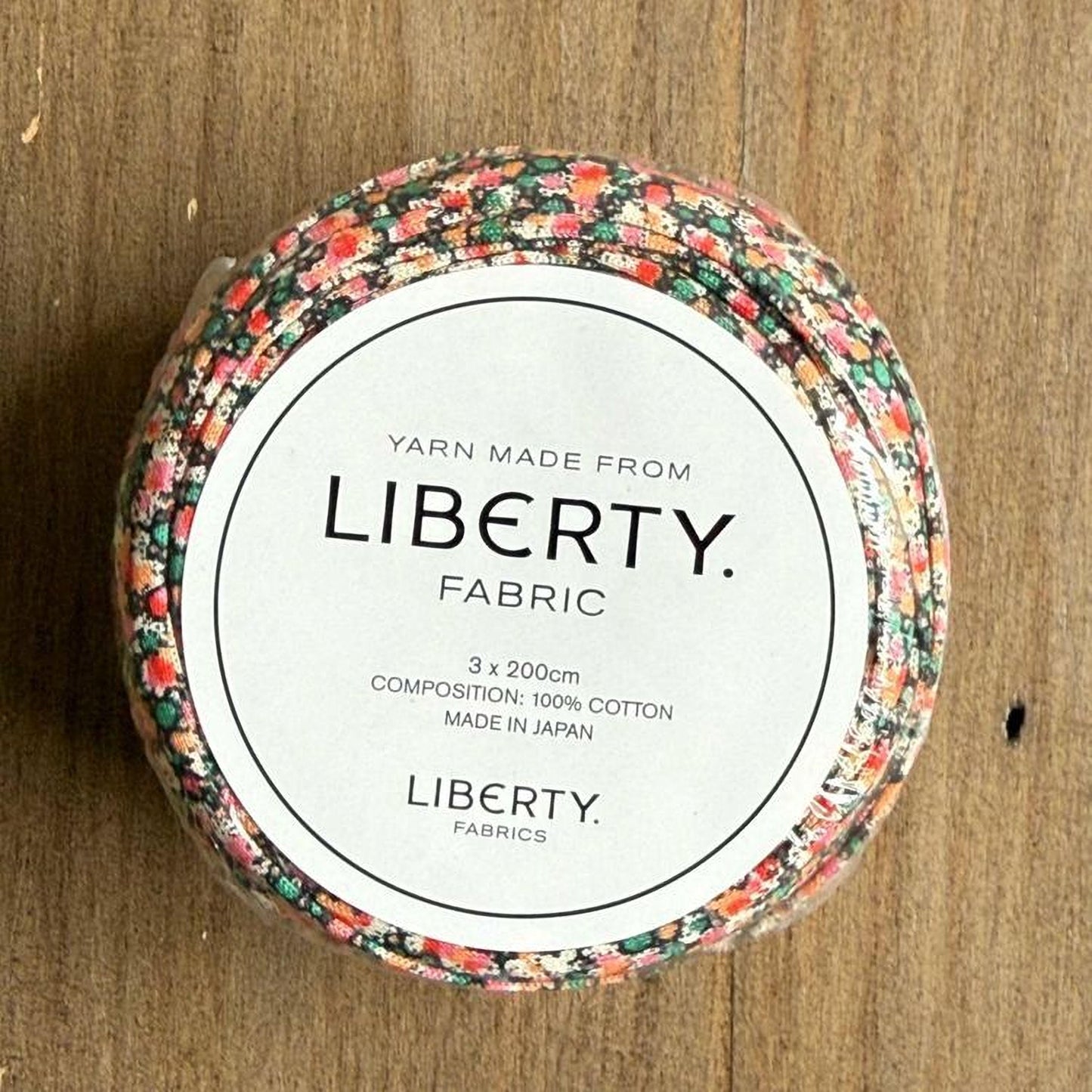 A spool of yarn with a floral pattern, labeled as "Liberty Fabric" and made from 100% cotton.