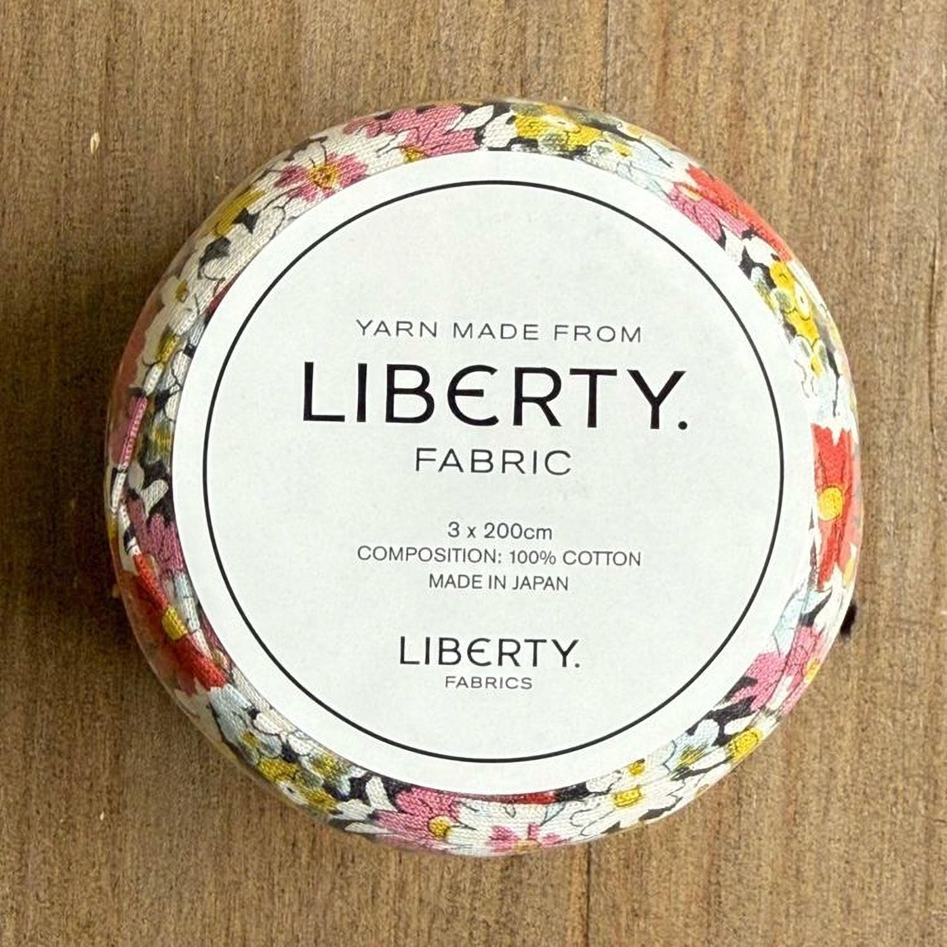 A round, white container with a floral pattern, labeled as "Yarn Made from Liberty. Fabric".