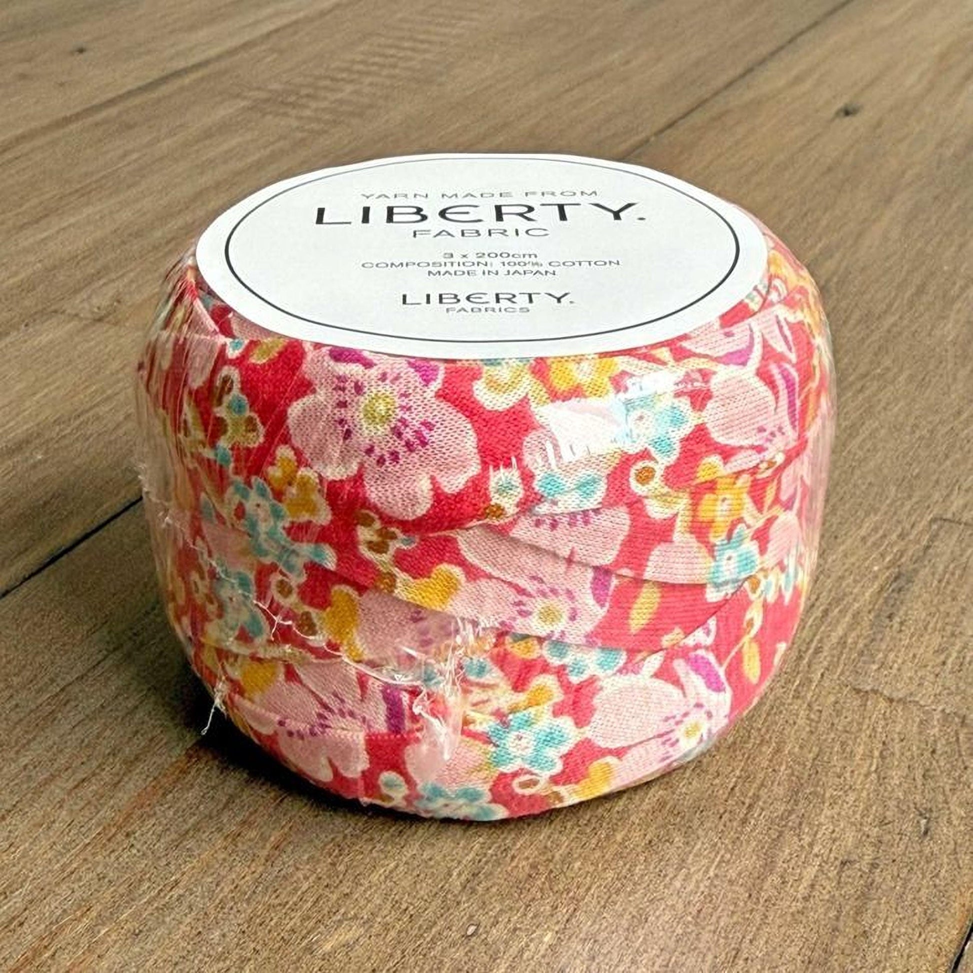 A roll of fabric with a floral pattern, sitting on a wooden surface.
